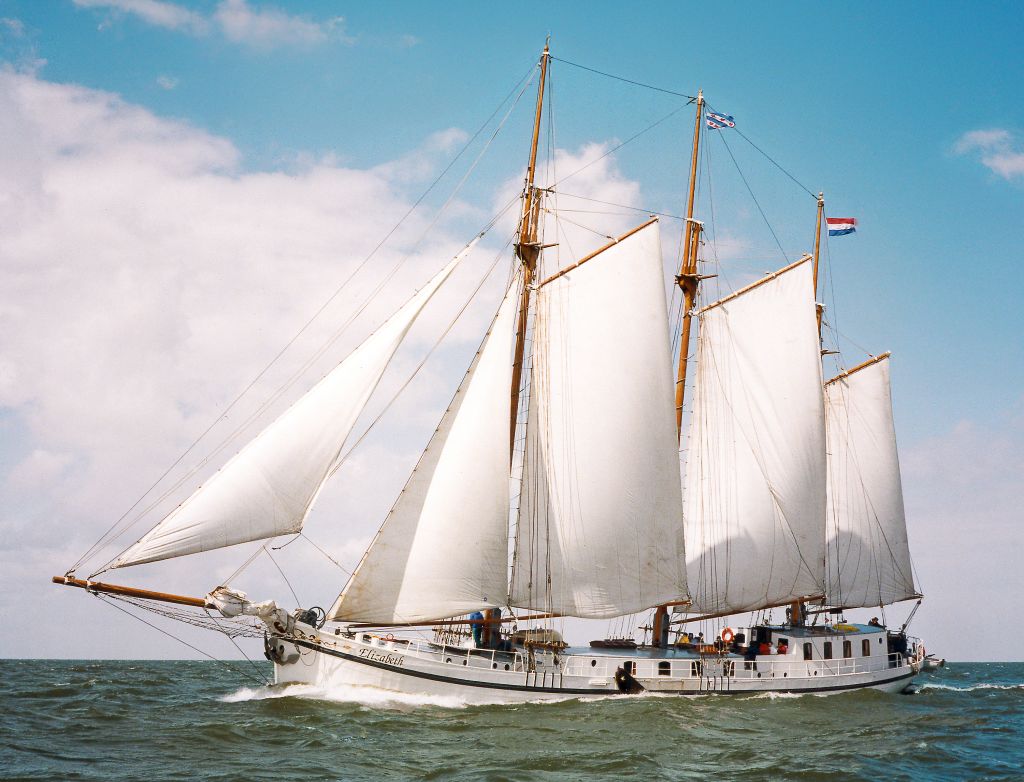 Nave a vela classica con tre alberi che naviga in mare aperto, cielo sereno e bandiere al vento.