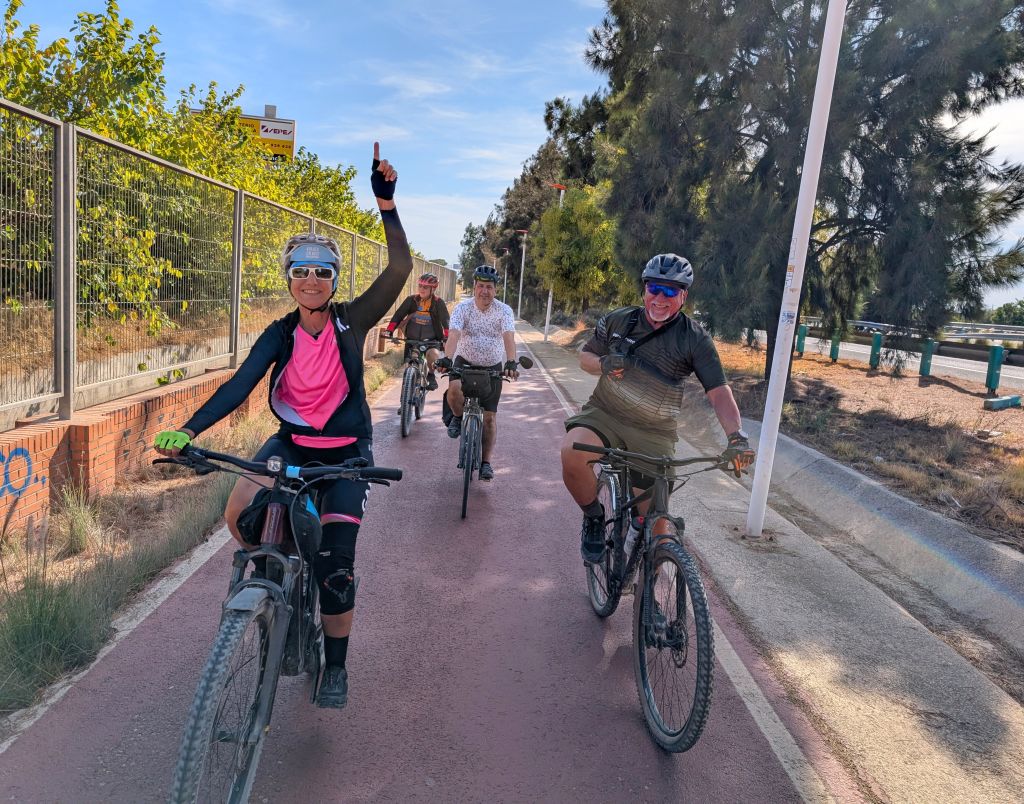 Ciclisti su una pista ciclabile ombreggiata nel lungomare di una località costiera spagnola.