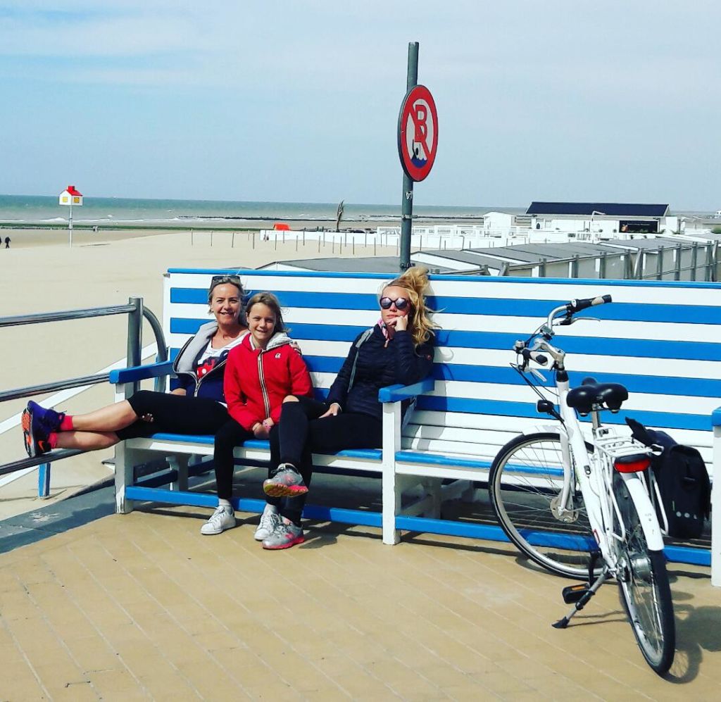 Famiglia in pausa seduta su una grande panchina con vista sul mare, vacanze in bici per famiglie "Girolibero"