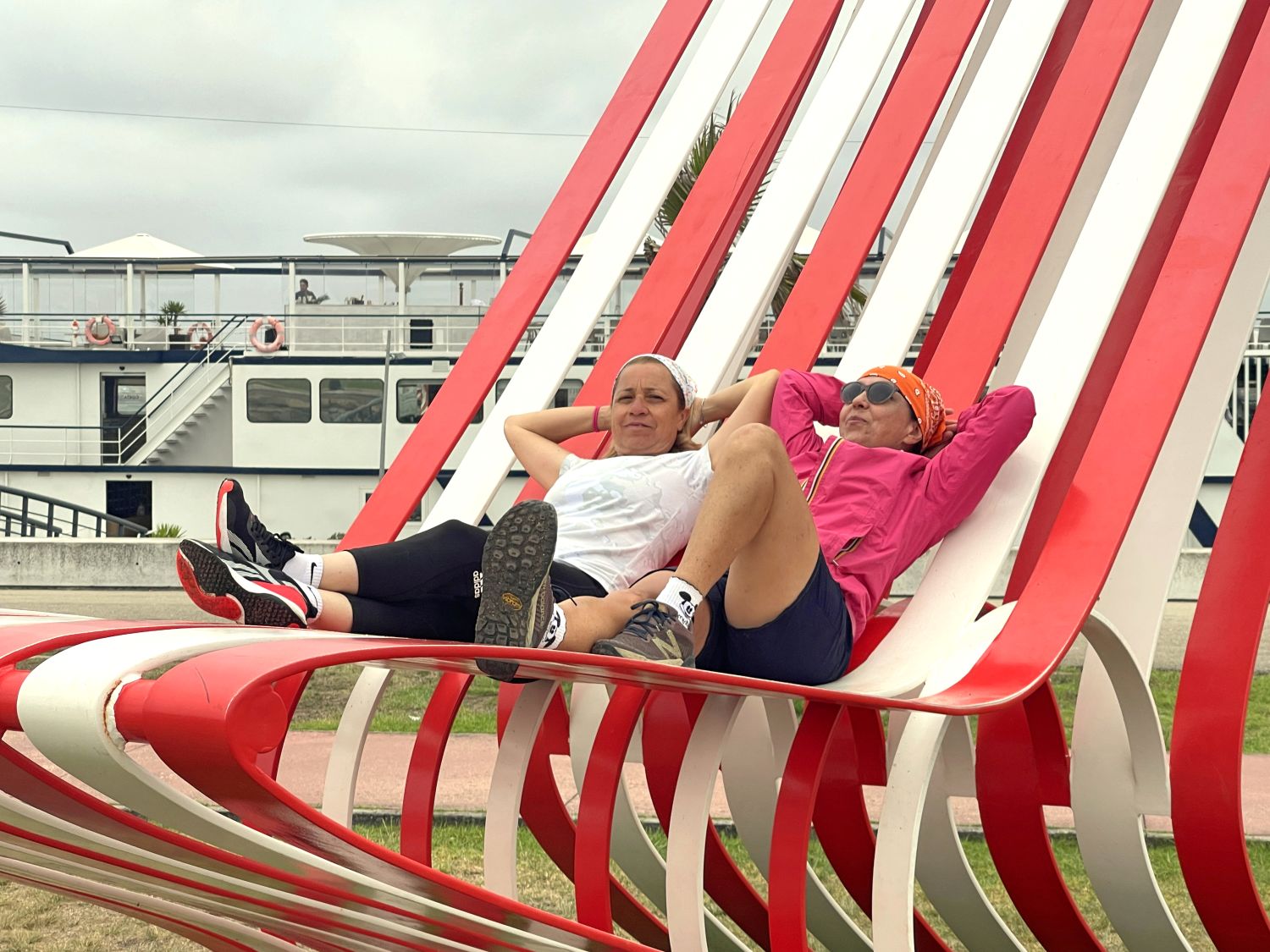 Cicliste in viaggio con Girolibero rilassate su grandi sculture urbane rosse a forma di poltrona