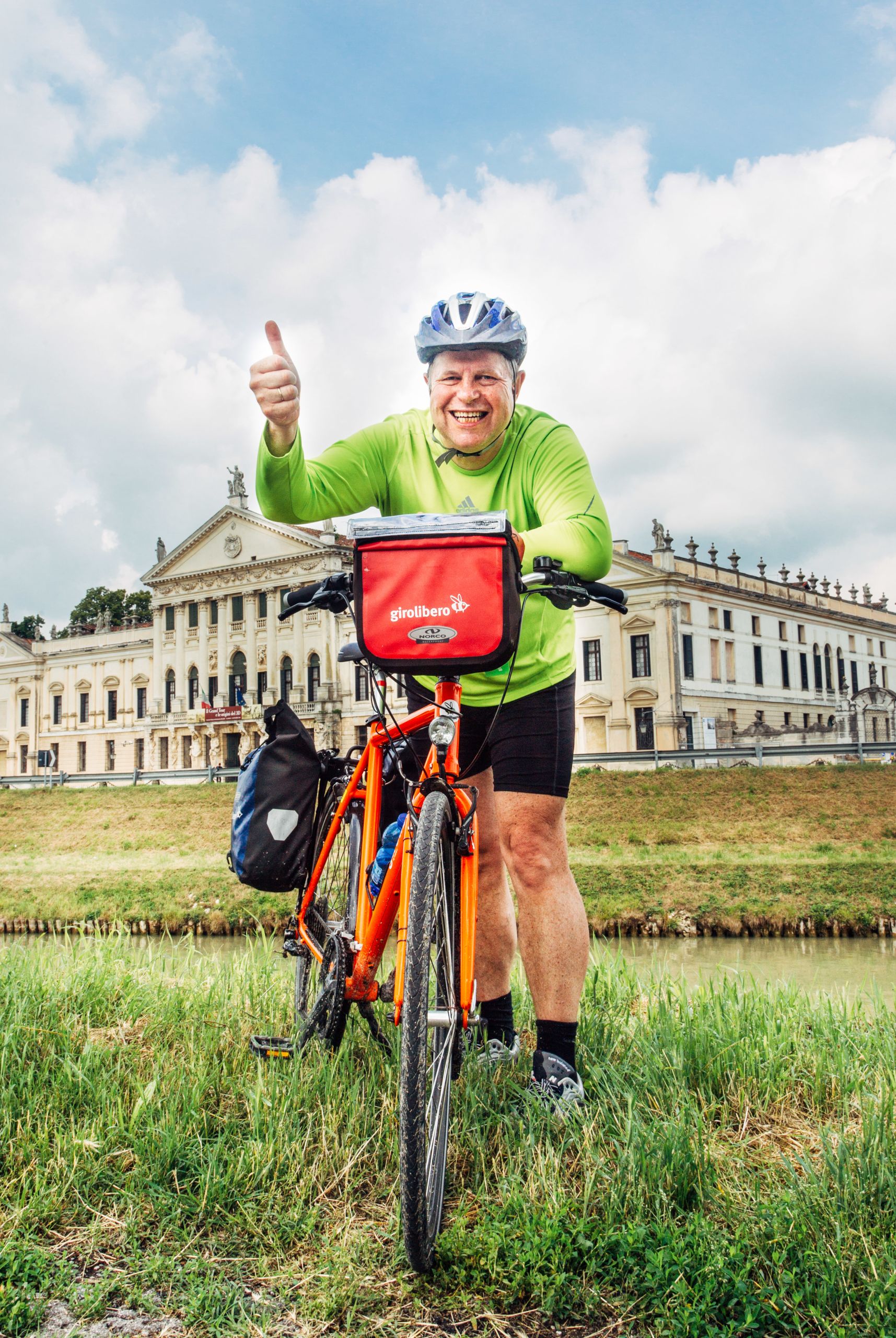 Lächelnder Radfahrer mit erhobenem Daumen, Helm und muskulösem Fahrrad „Girolibero“, langsamer Tourismus, Radurlaub in Italien