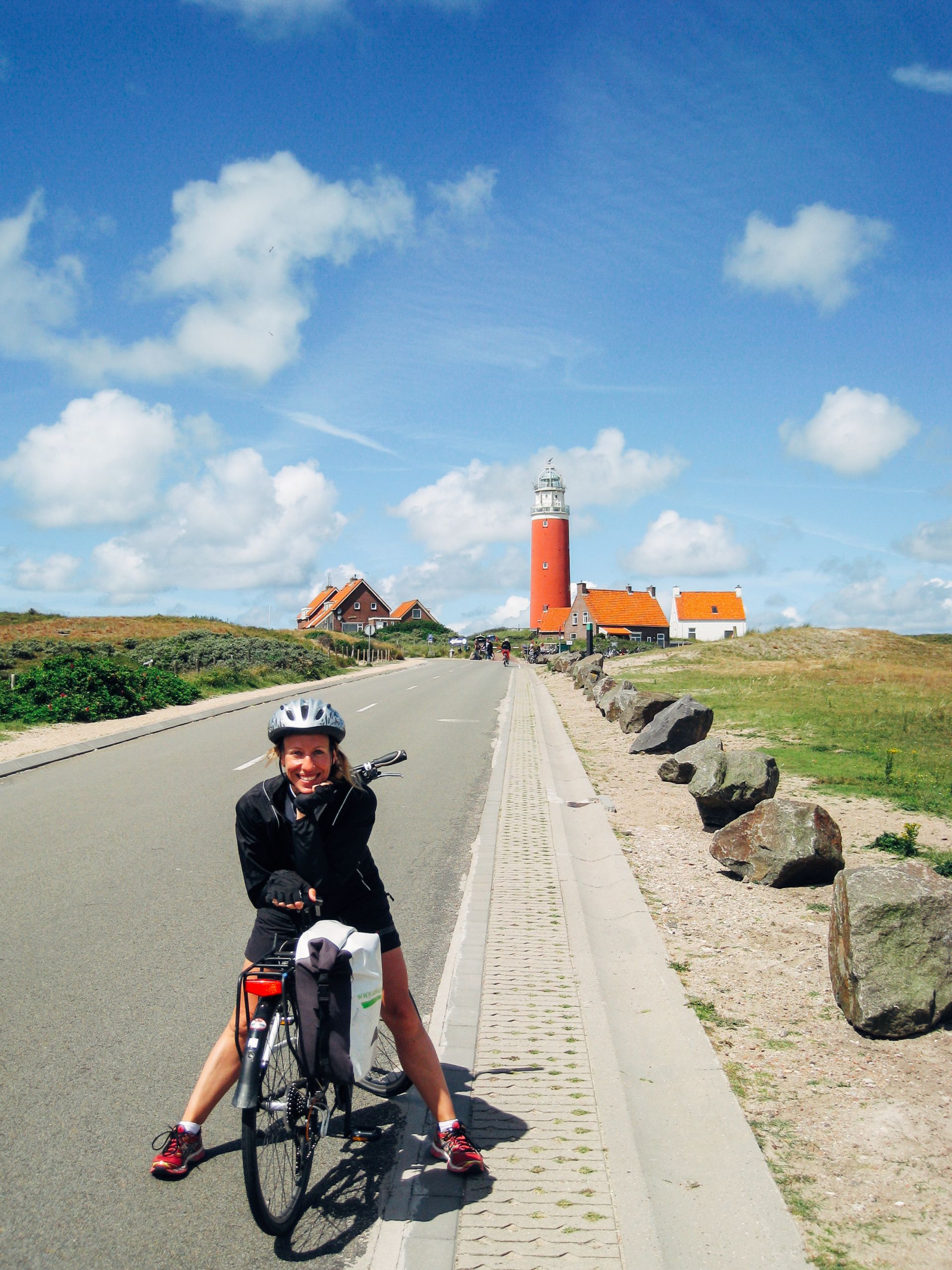 Radfahrer auf einem Radweg entlang eines Kanals mit einem Leuchtturm in der Ferne, Texel
