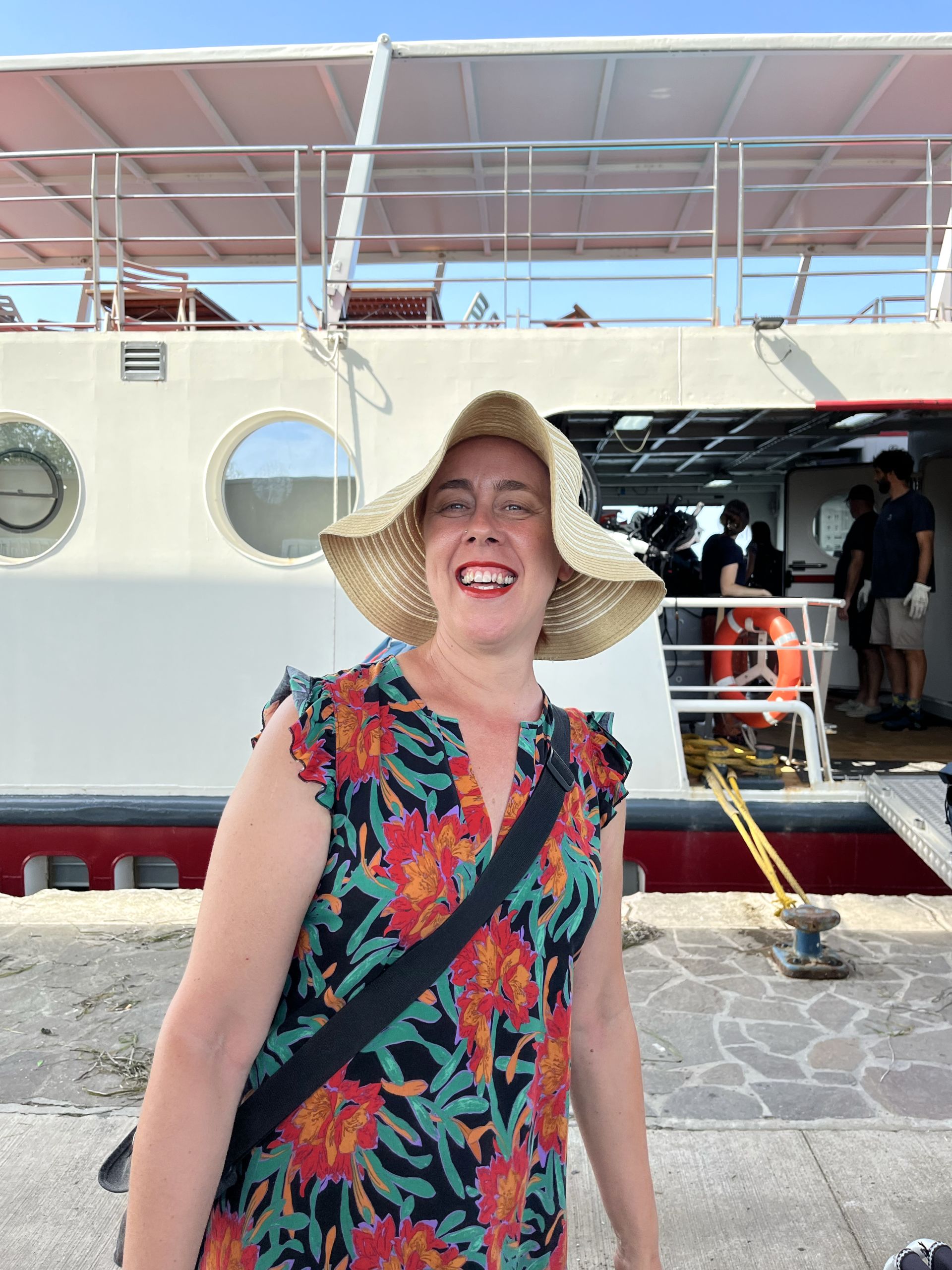 Smiling tourist with wide-brimmed hat on cruise ship deck.