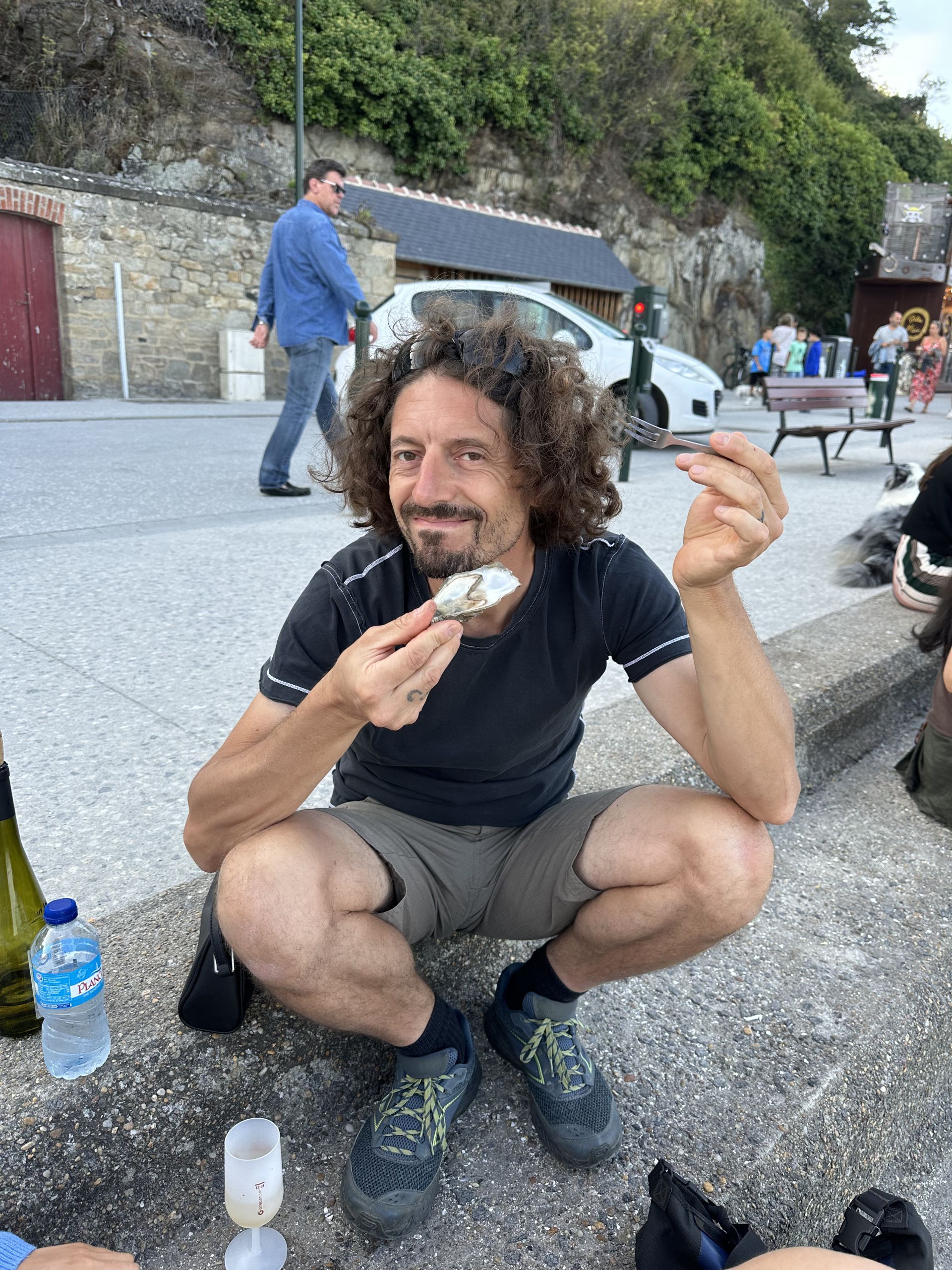 Uomo sorridente mentre mangia un'ostrica fresca in una piazza, vicino al mercato del pesce.