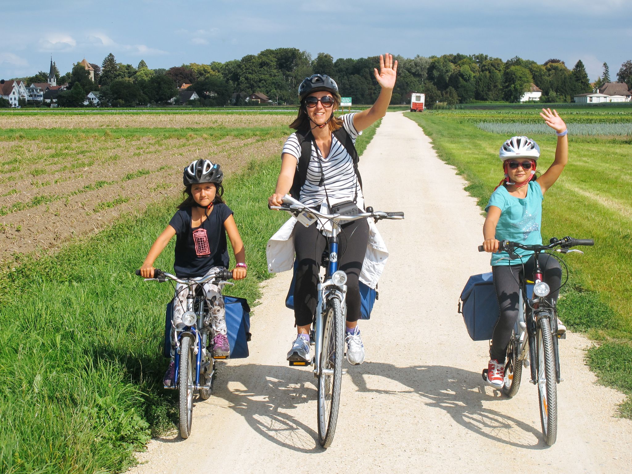 Famiglia di cicloturisti, bambine con caschetto, bici bimbo, paesaggio verde coltivato, divertimento, lago di Costanza
