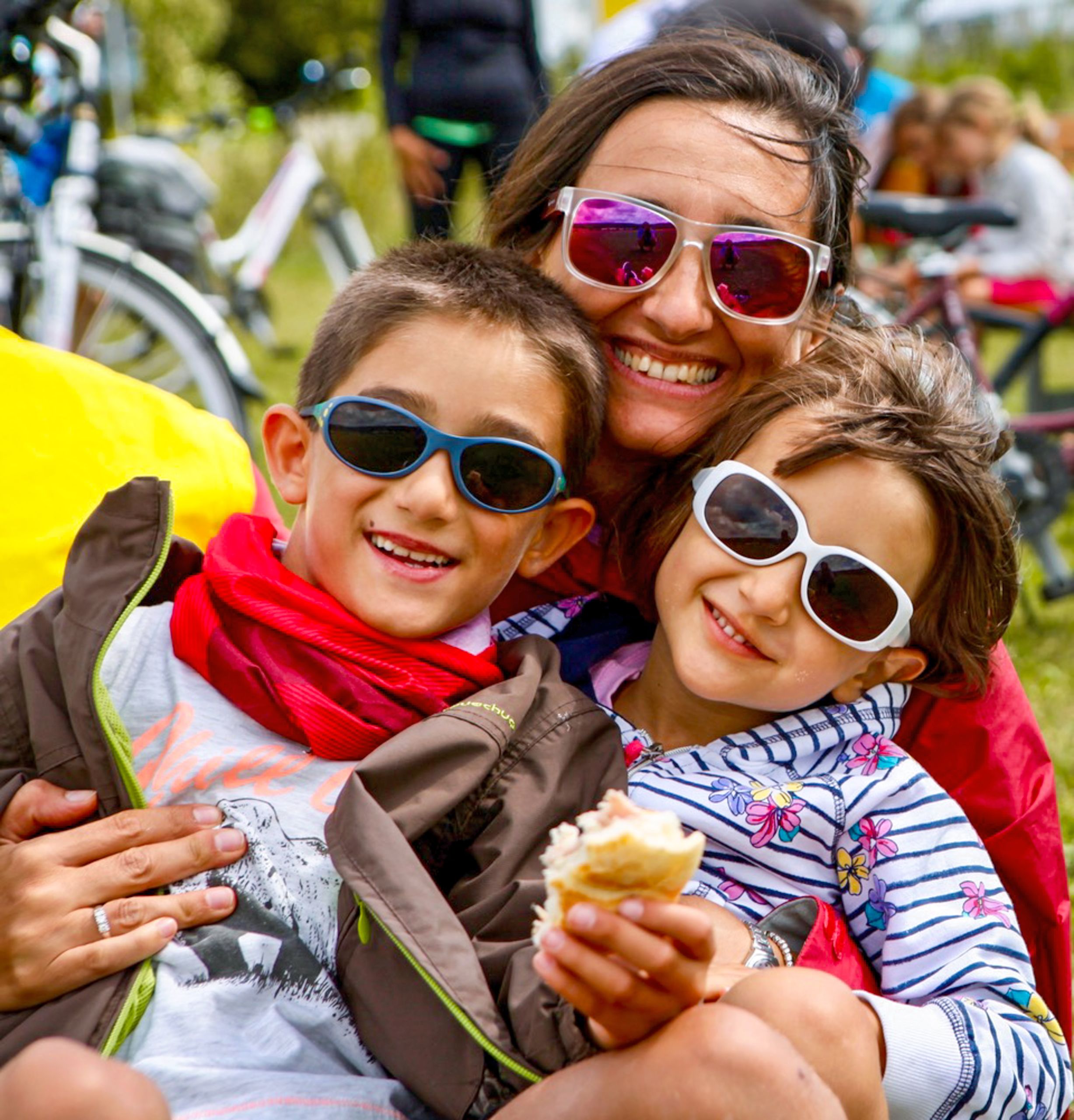 Mamma con due bambini sorridenti in bici, tutti con occhiali da sole, vacanza in bici con Girolibero.