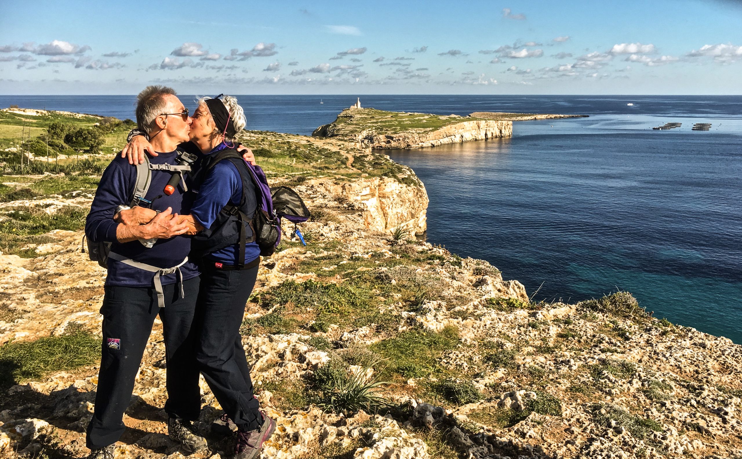 Coppia abbracciata su una scogliera rocciosa con vista sul mare, trekking organizzato da Gozo a La Valletta.