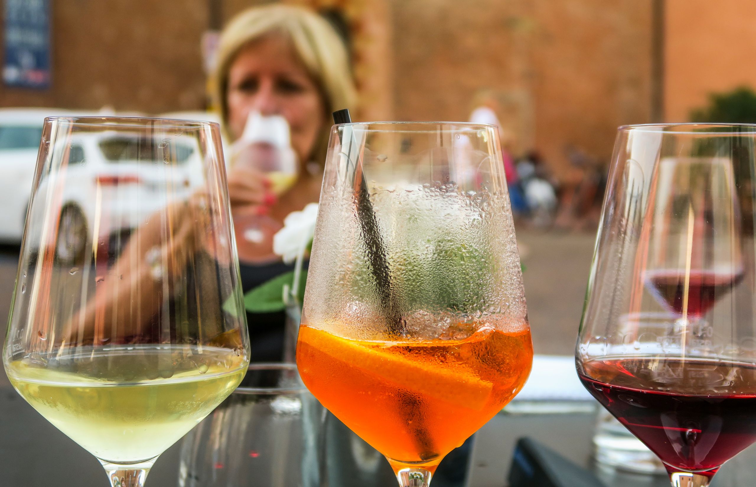 Tre bicchieri da aperitivo in primo piano, uno di vino bianco, uno spritz aperol, un bicchiere di Barolo, Piemonte