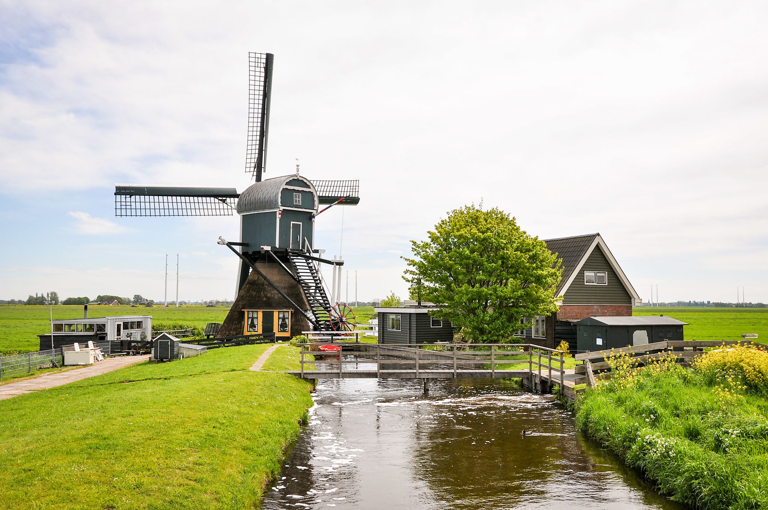 Traditionelle Windmühle in der Nähe eines Wasserwegs und grüner Felder, Niederlande