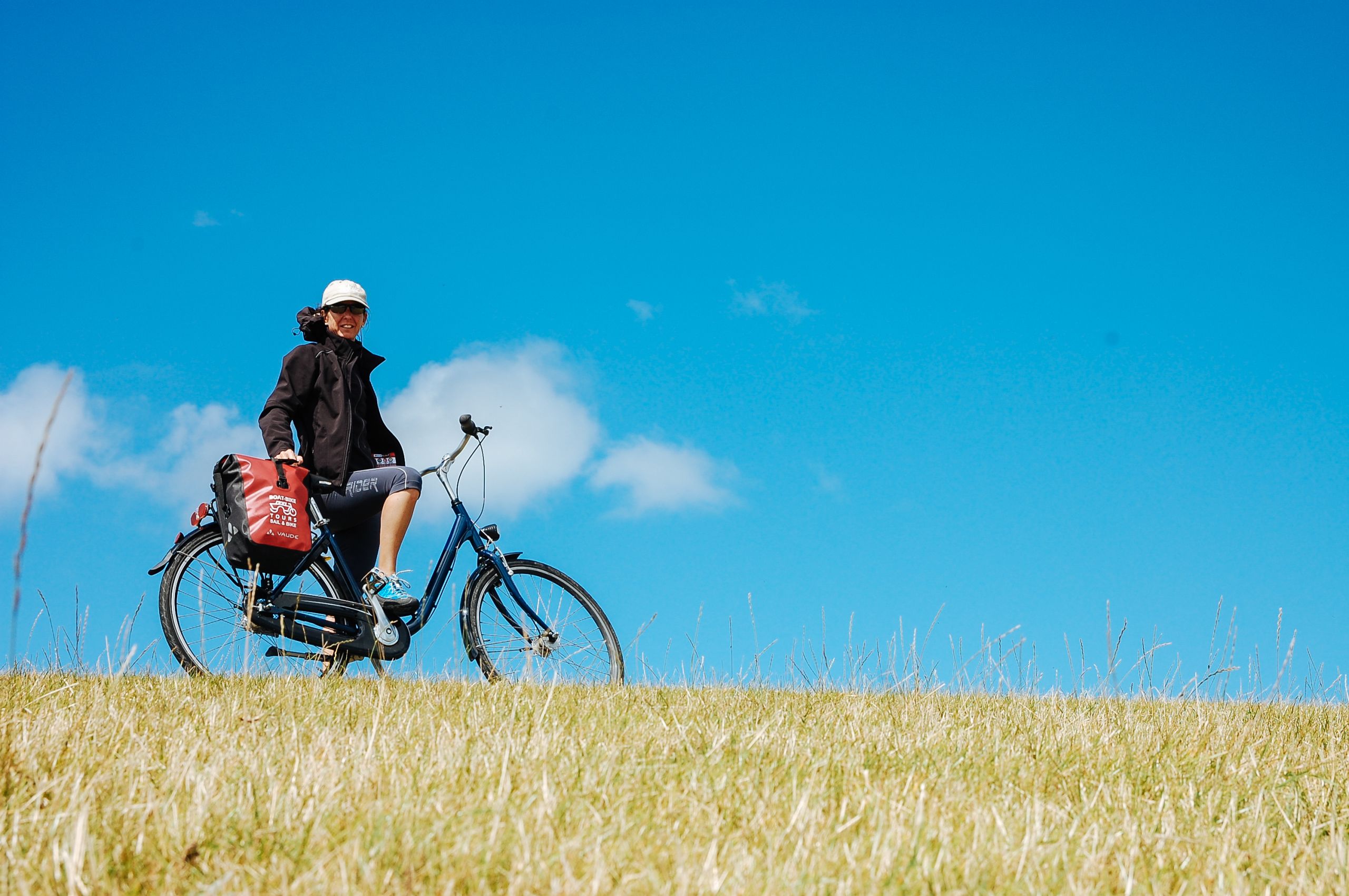Cyclist with bike and "Girolibero" bag admires the green panorama during a cycling tour in the West Frisian Islands, Netherlands