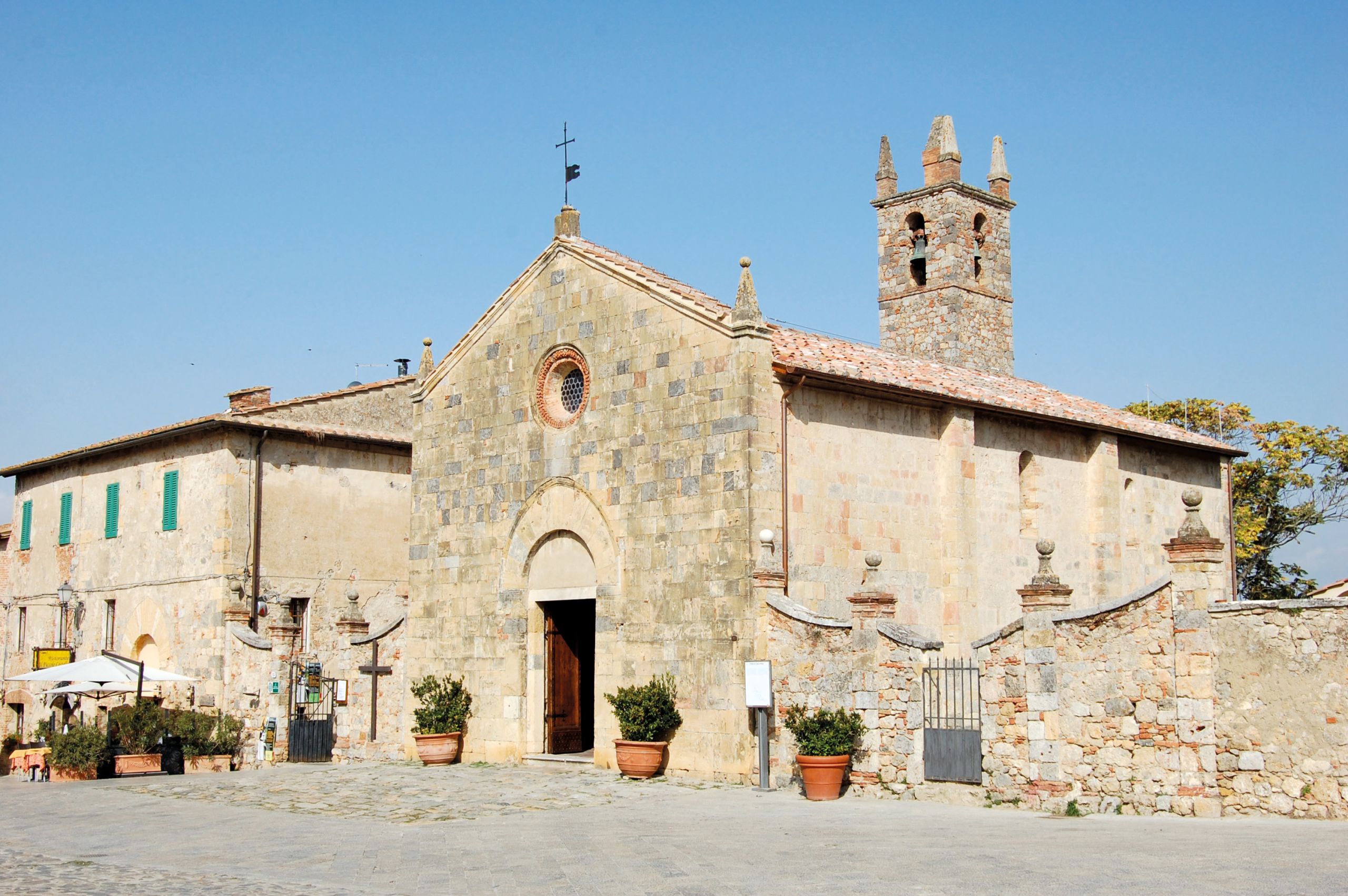 Historische Steinkirche mit sonnigem Platz in einem toskanischen Dorf.