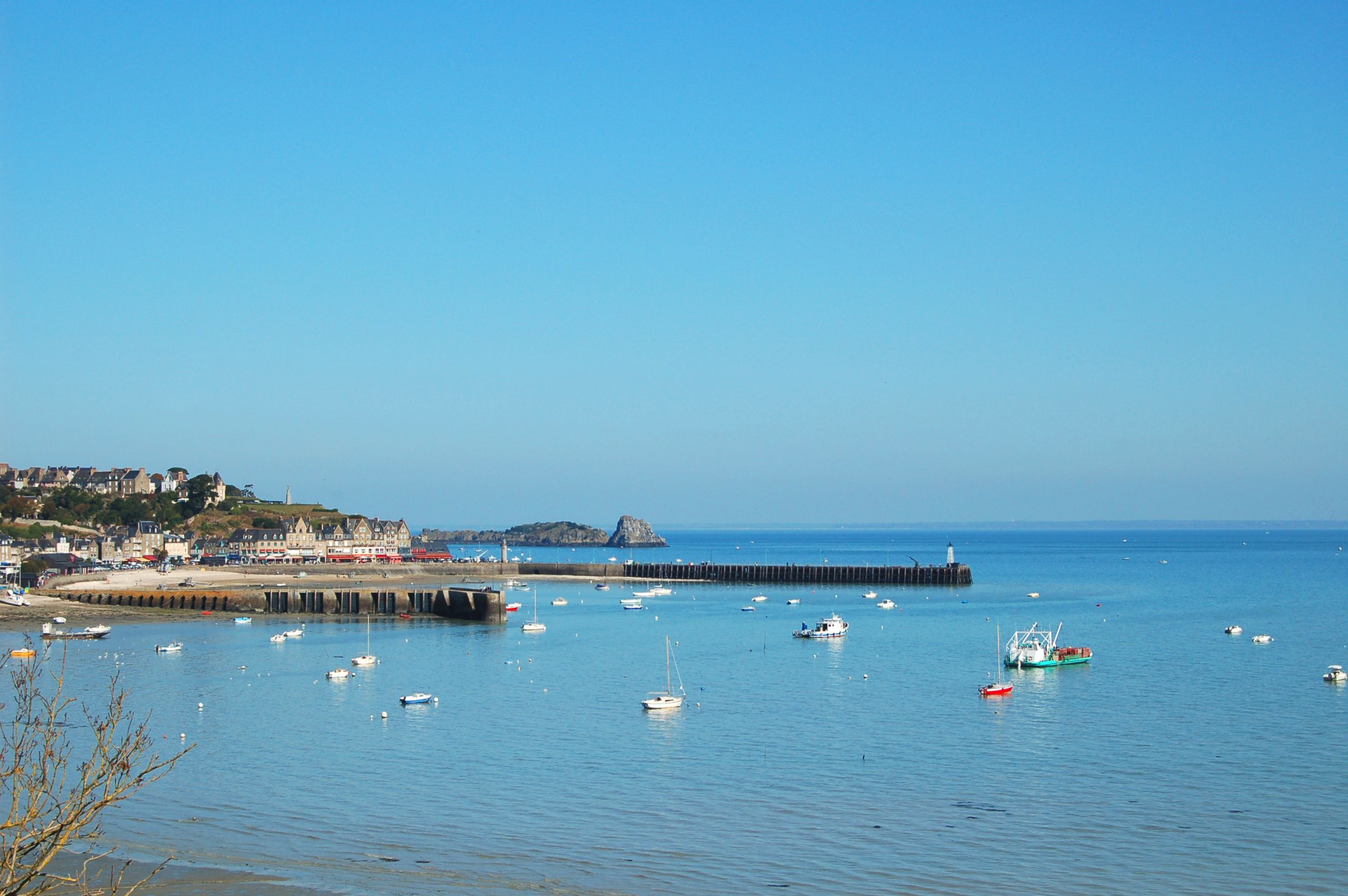 Barche ormeggiate in un piccolo porto bretone con acqua cristallina e cielo azzurro.