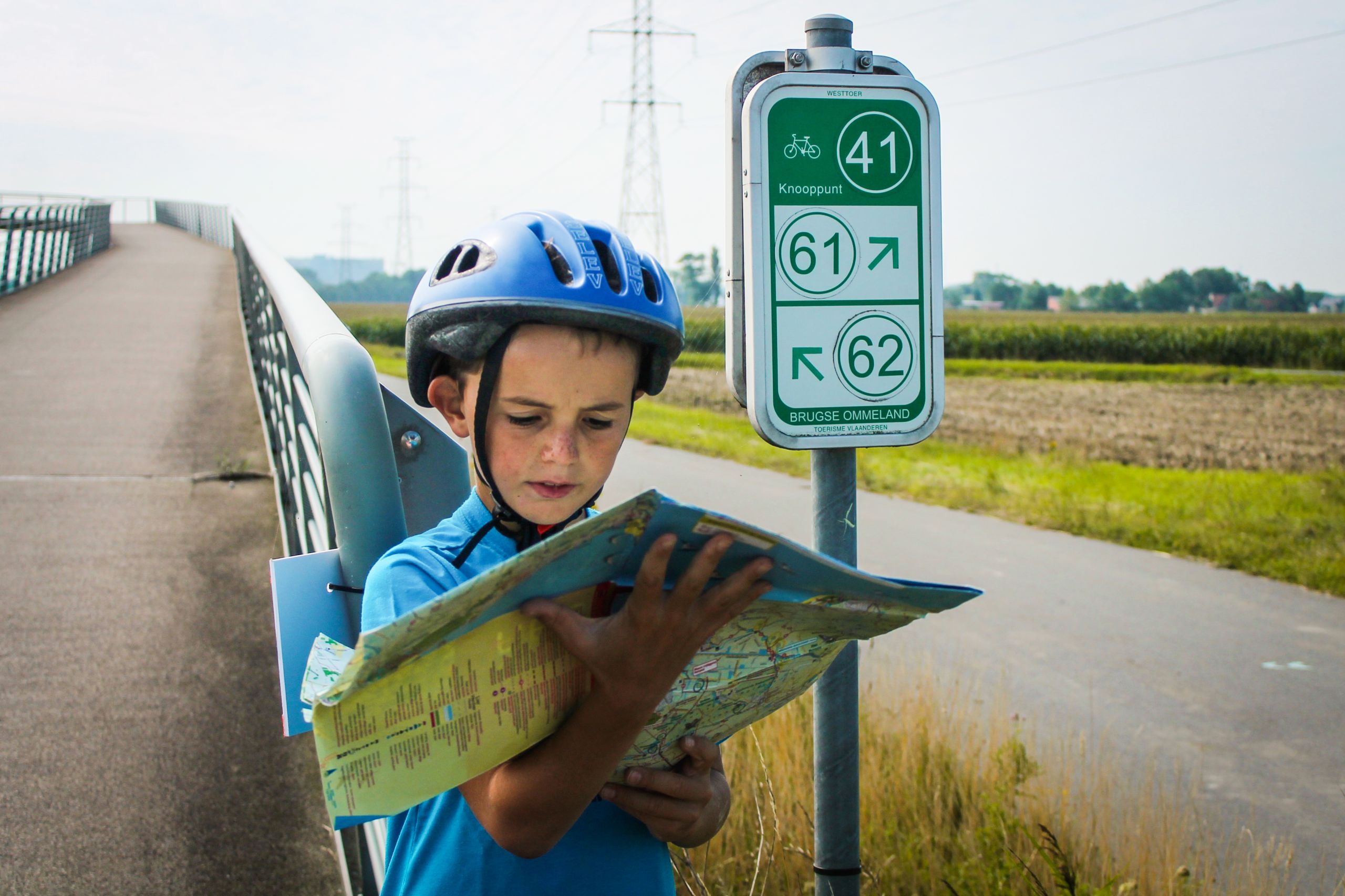 Bambino con caschetto legge una mappa ciclabile, vacanza in bici, Belgio