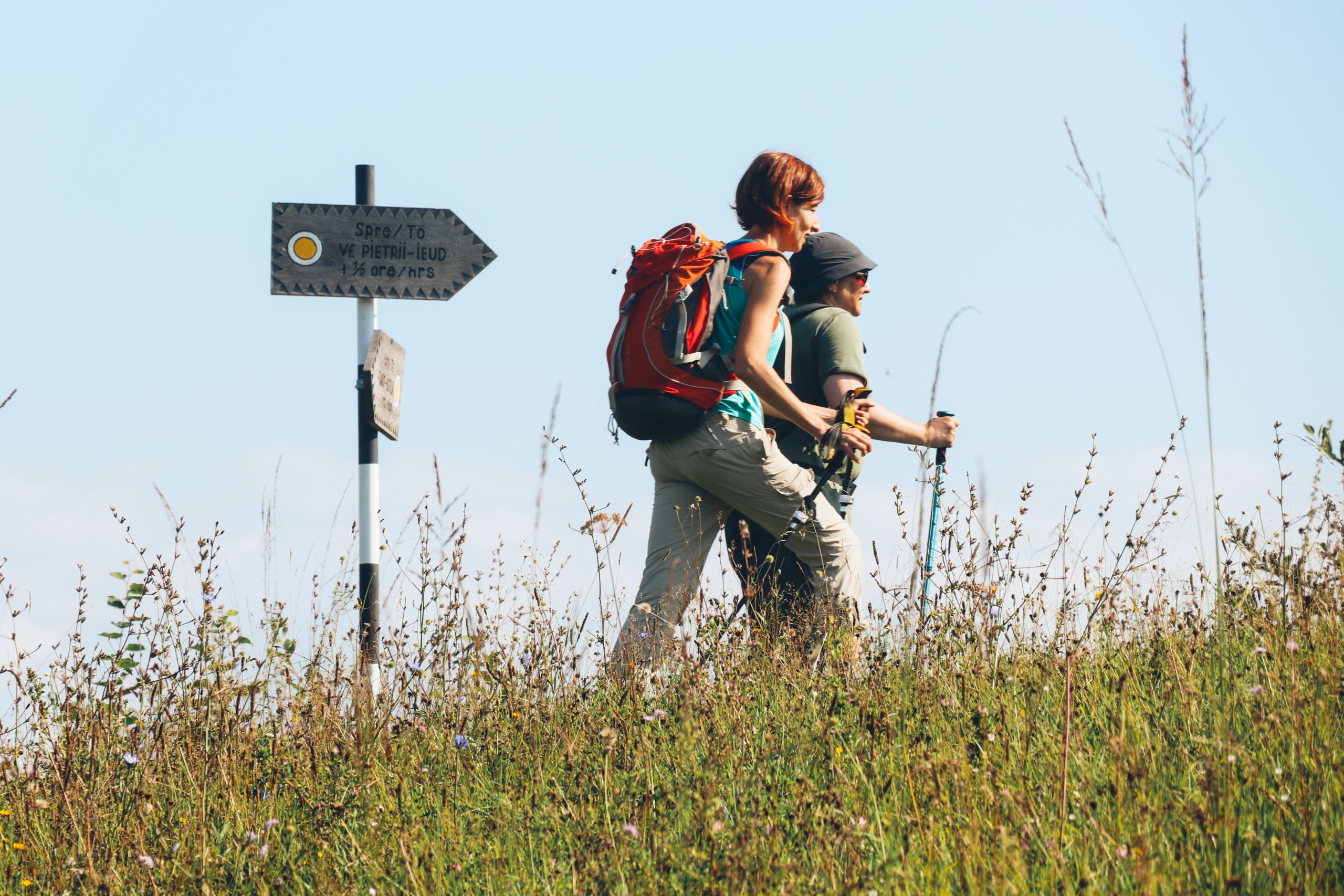 Due escursionisti passano vicino a un cartello con segnaletica lungo un percorso a piedi nelle montagne della Romania