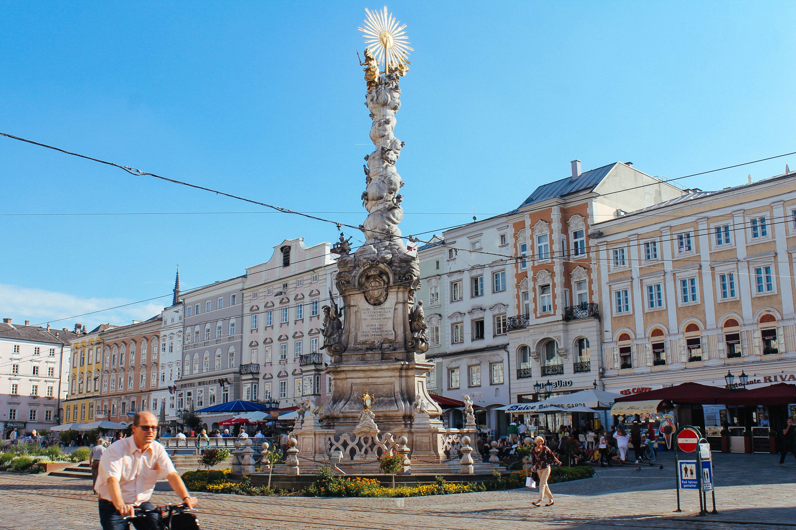 Piazza principale del centro storico di Linz, fontana, negozi, persone a passeggio e in bici, Austria