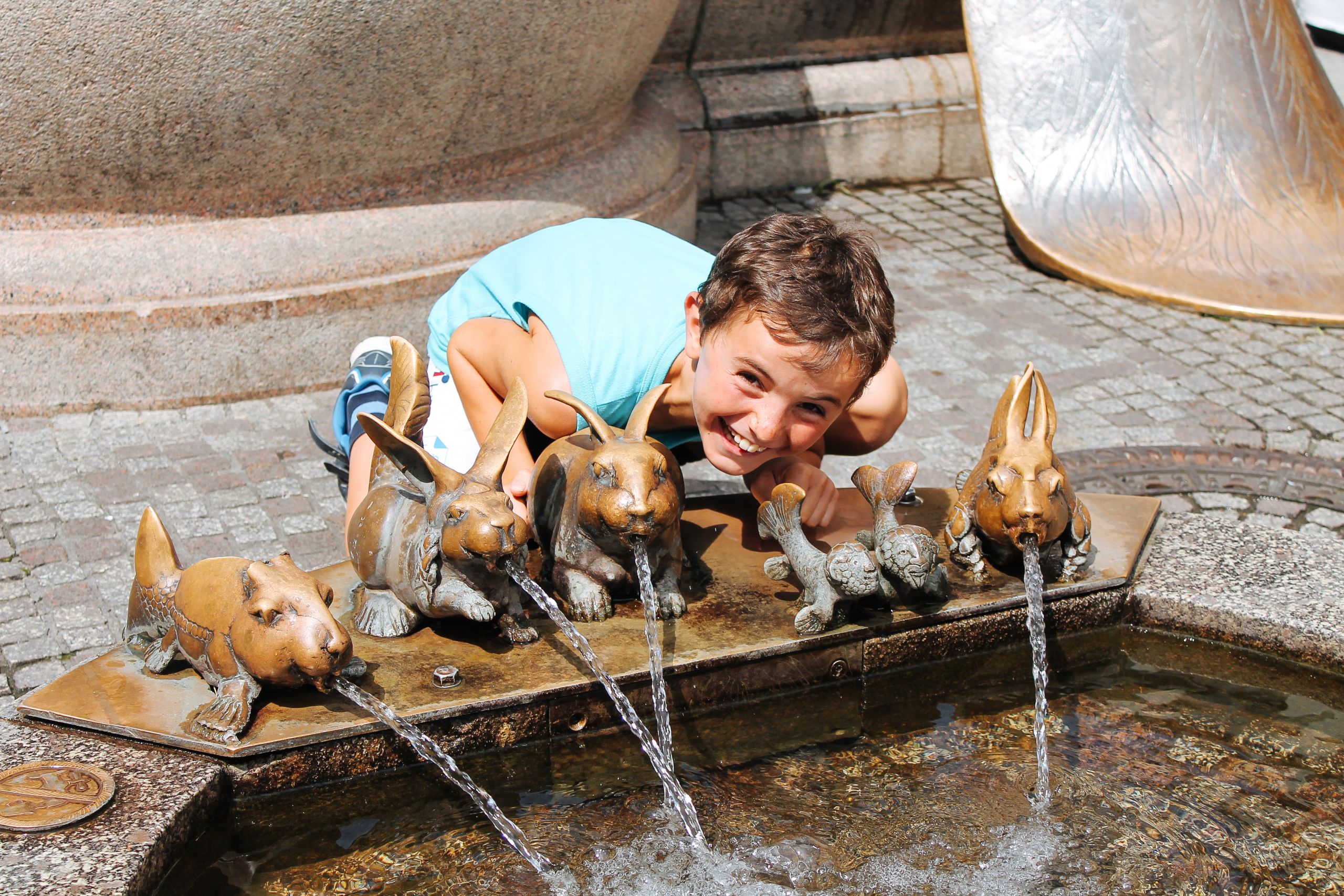 Bambino appoggiato a delle fontanelle d'acqua a forma di animaletti, vacanza all'aria aperta lungo il lago di Costanza