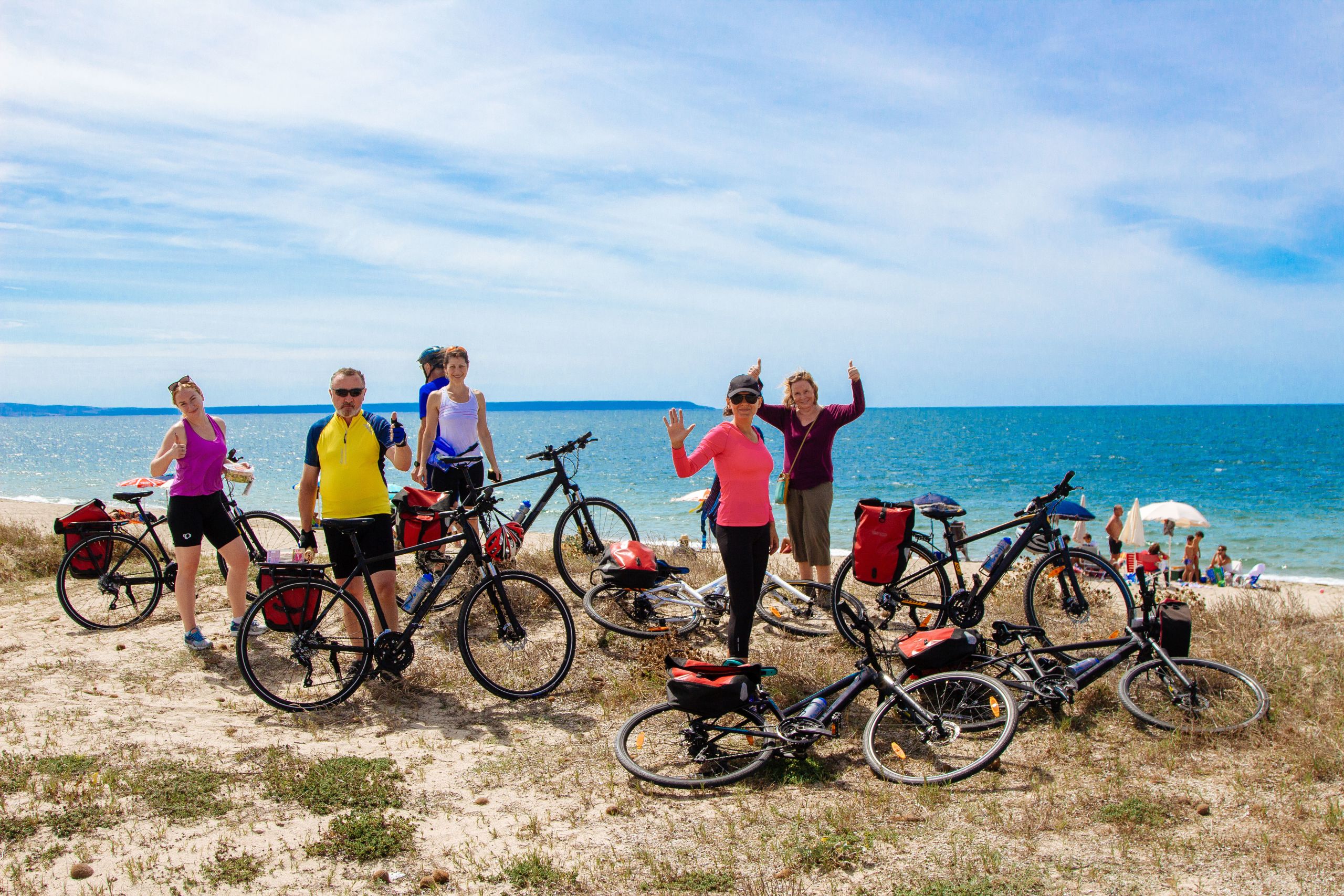 Gruppo di ciclisti in con biciclette in posa su uno scoglio davanti al mare, vacanze in bici in Sardegna