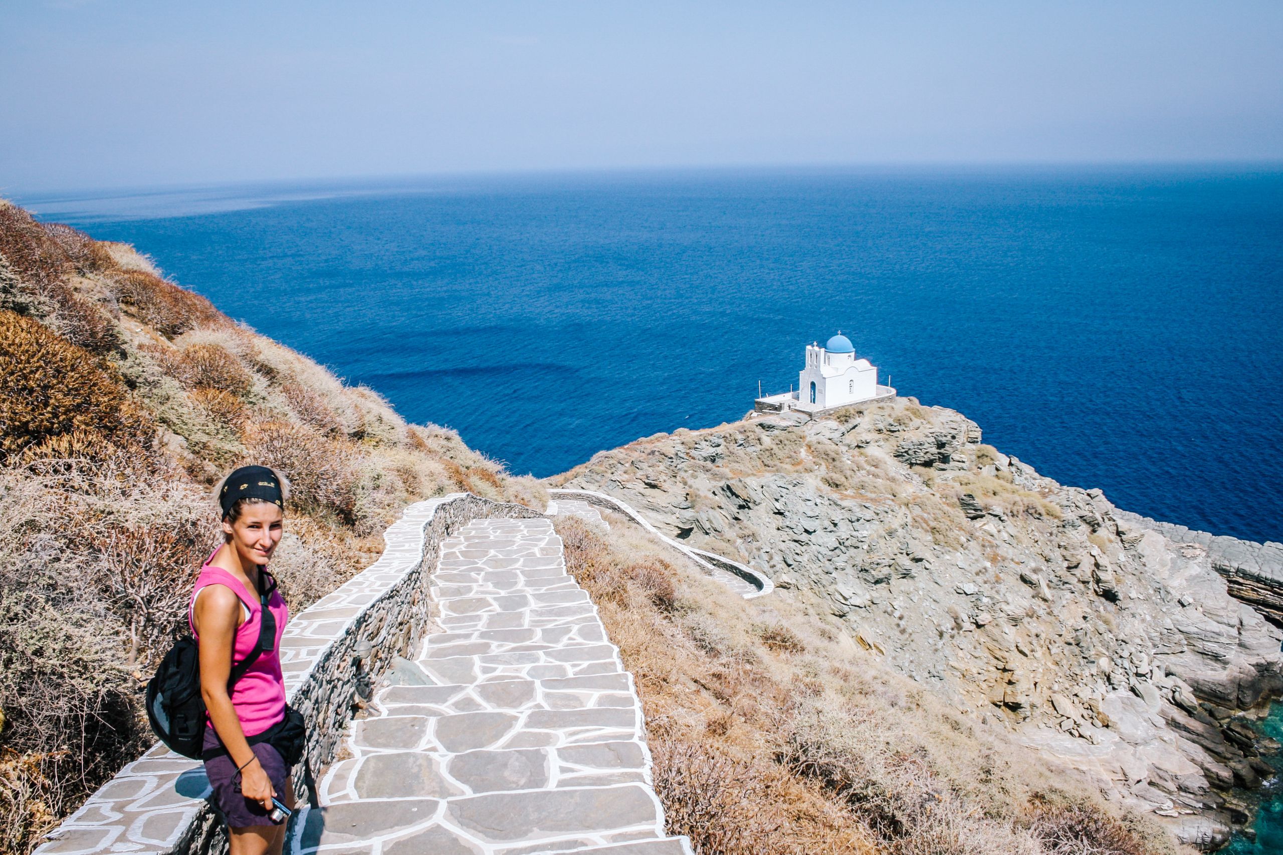 Escursionista su un sentiero con vista sul mare e cappella di Profitis Ilias, Grecia
