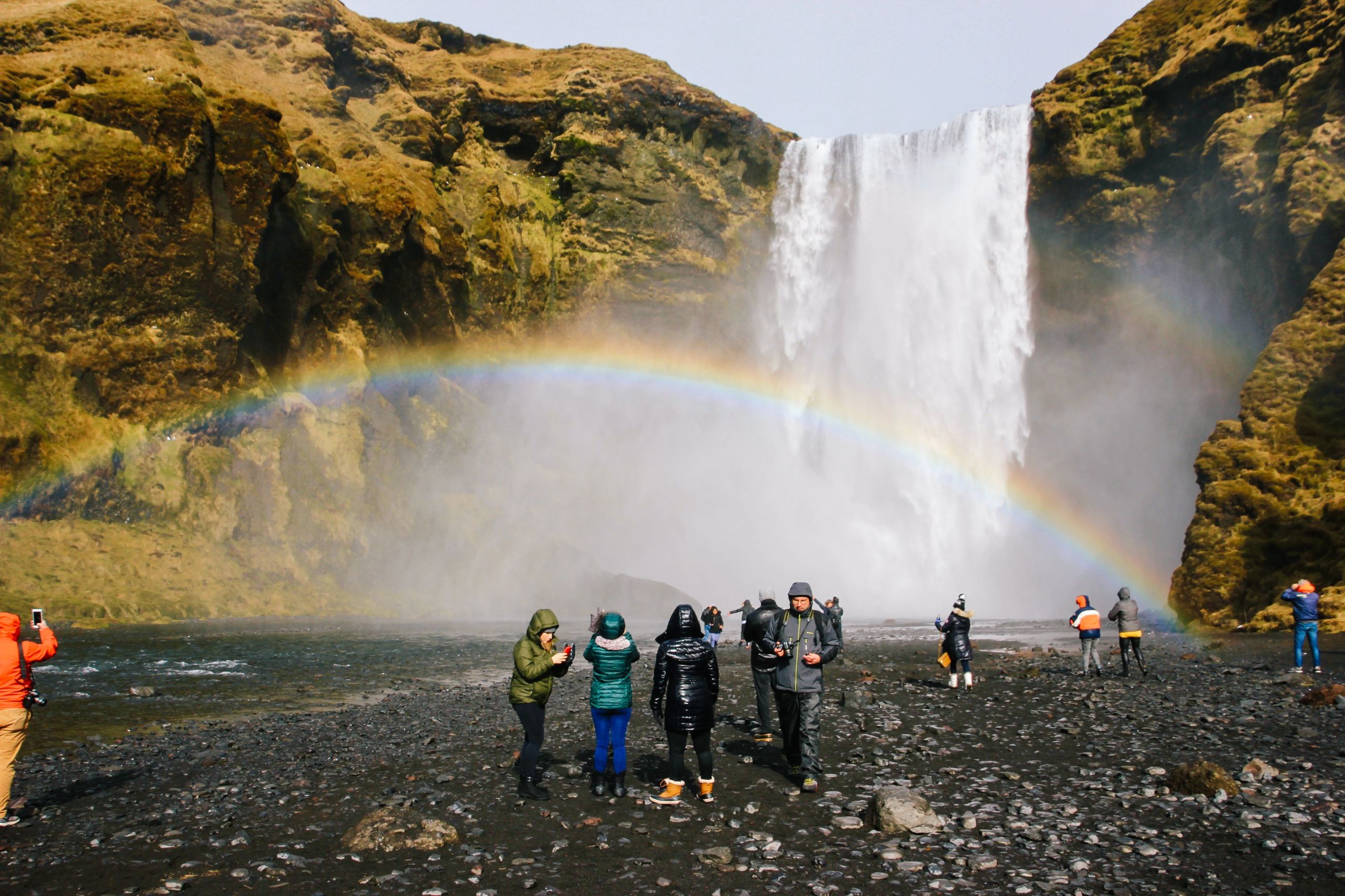 Turisti che osservano la cascata Skógafoss con un arcobaleno al centro della scena, Islanda.