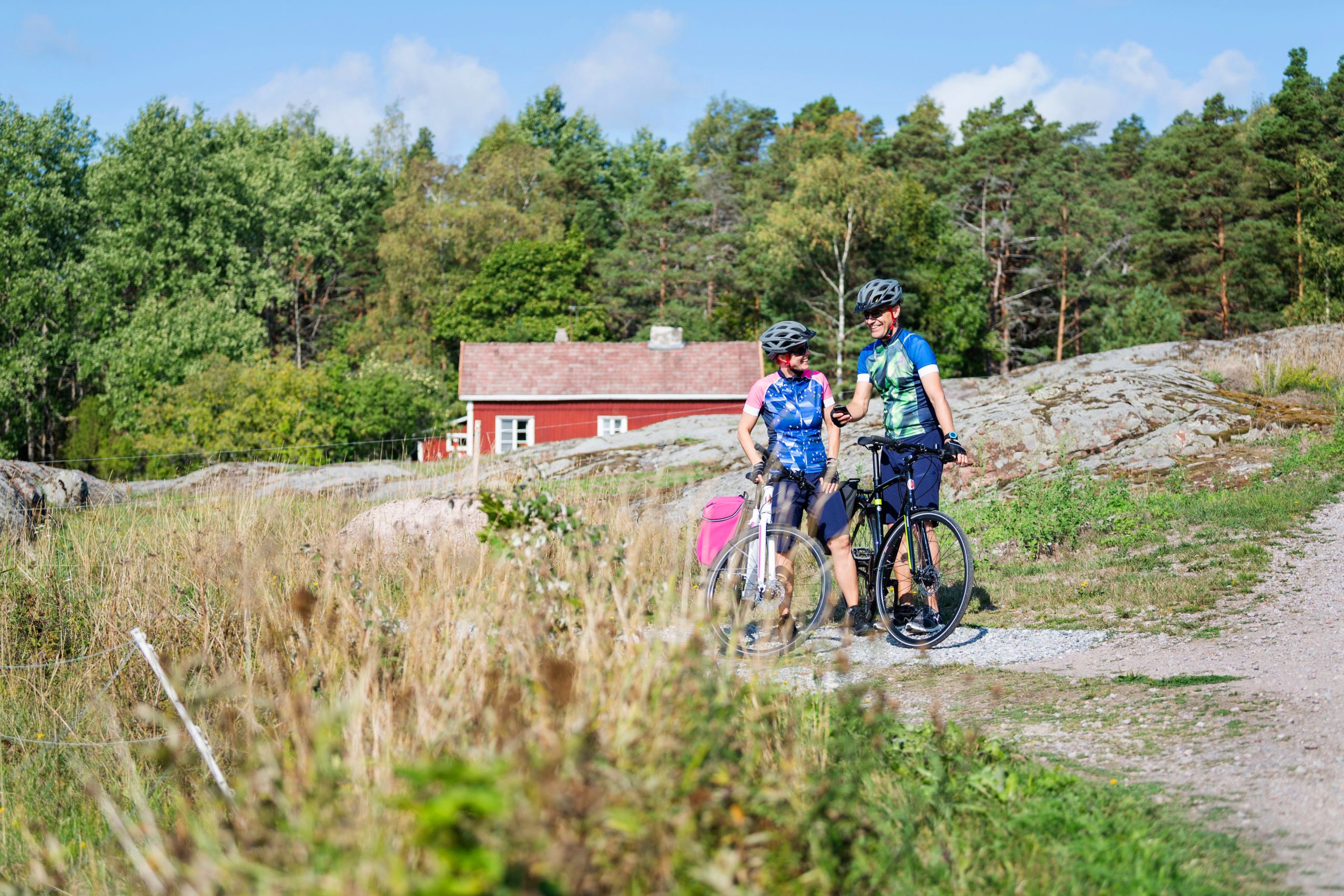 Coppia in bicicletta su una strada sterrata vicino a una casa rossa tradizionale finlandese tra i boschi