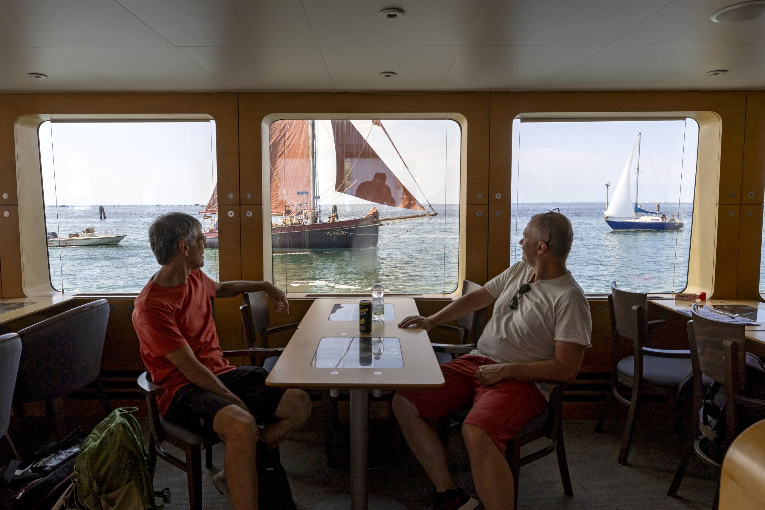 Coppia seduta al tavolo interno della barca con finestre con vista sul mare