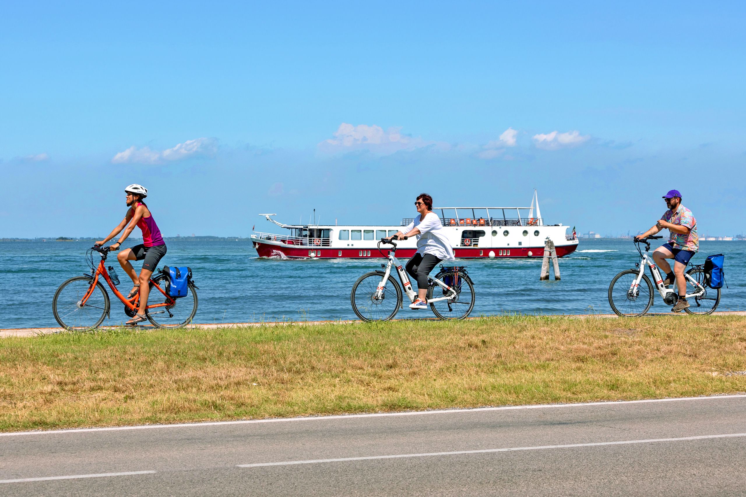 Ciclisti che pedalano lungo una pista ciclabile vicino al mare sotto un cielo azzurro, viaggi in bici e barca organizzati "Girolibero"