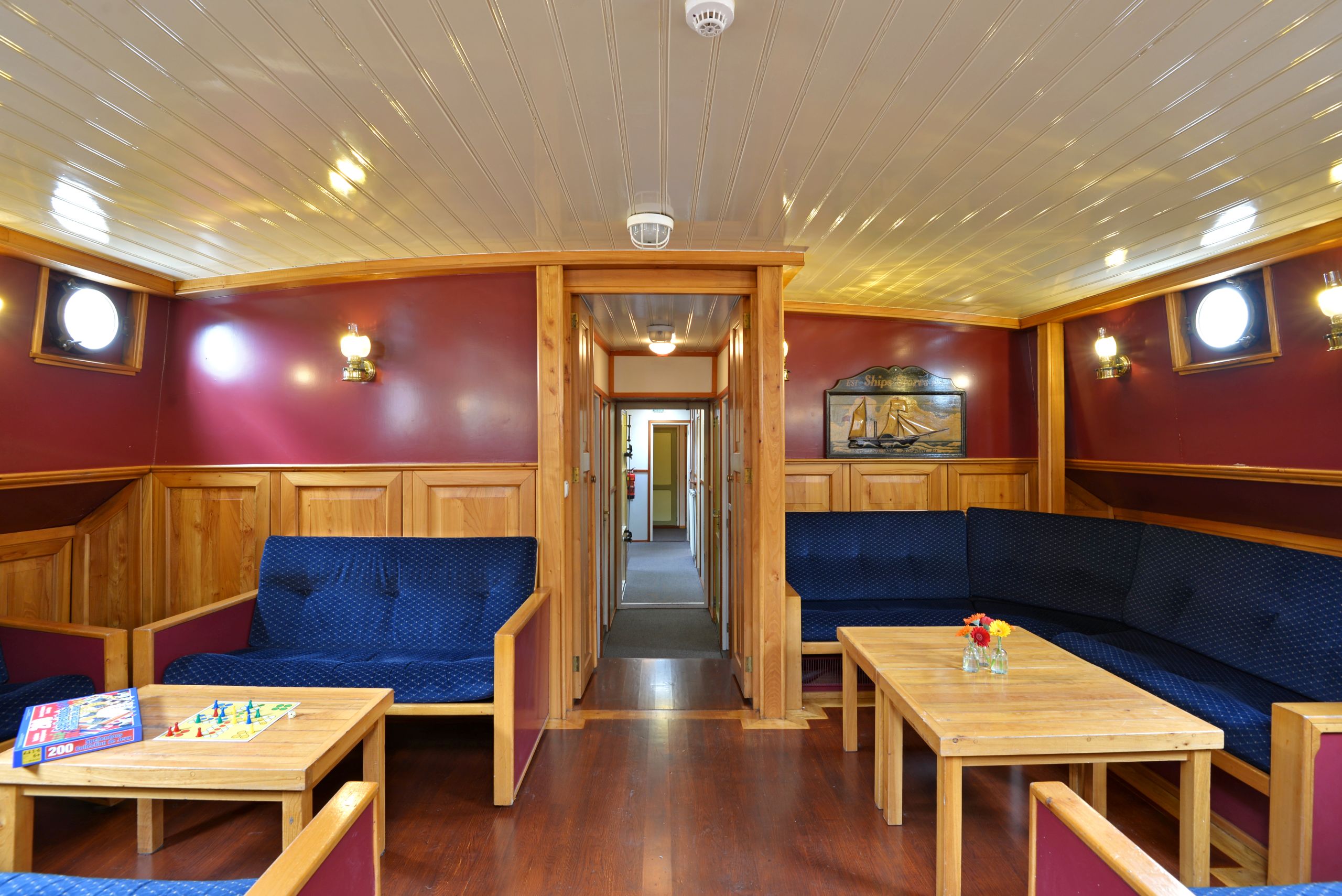 Sala comune con divani blu imbottiti, tavoli in legno e luci calde, perfetta per relax a bordo.