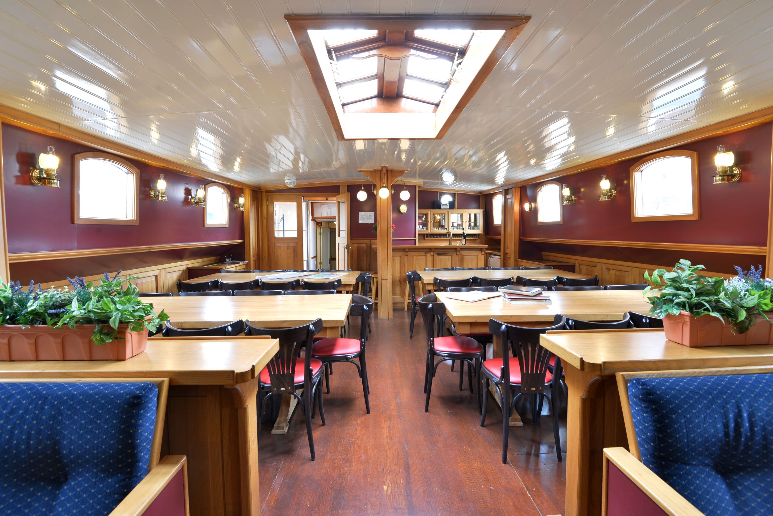 Sala da pranzo interna della nave con tavoli apparecchiati, sedili imbottiti blu e ampie finestre.