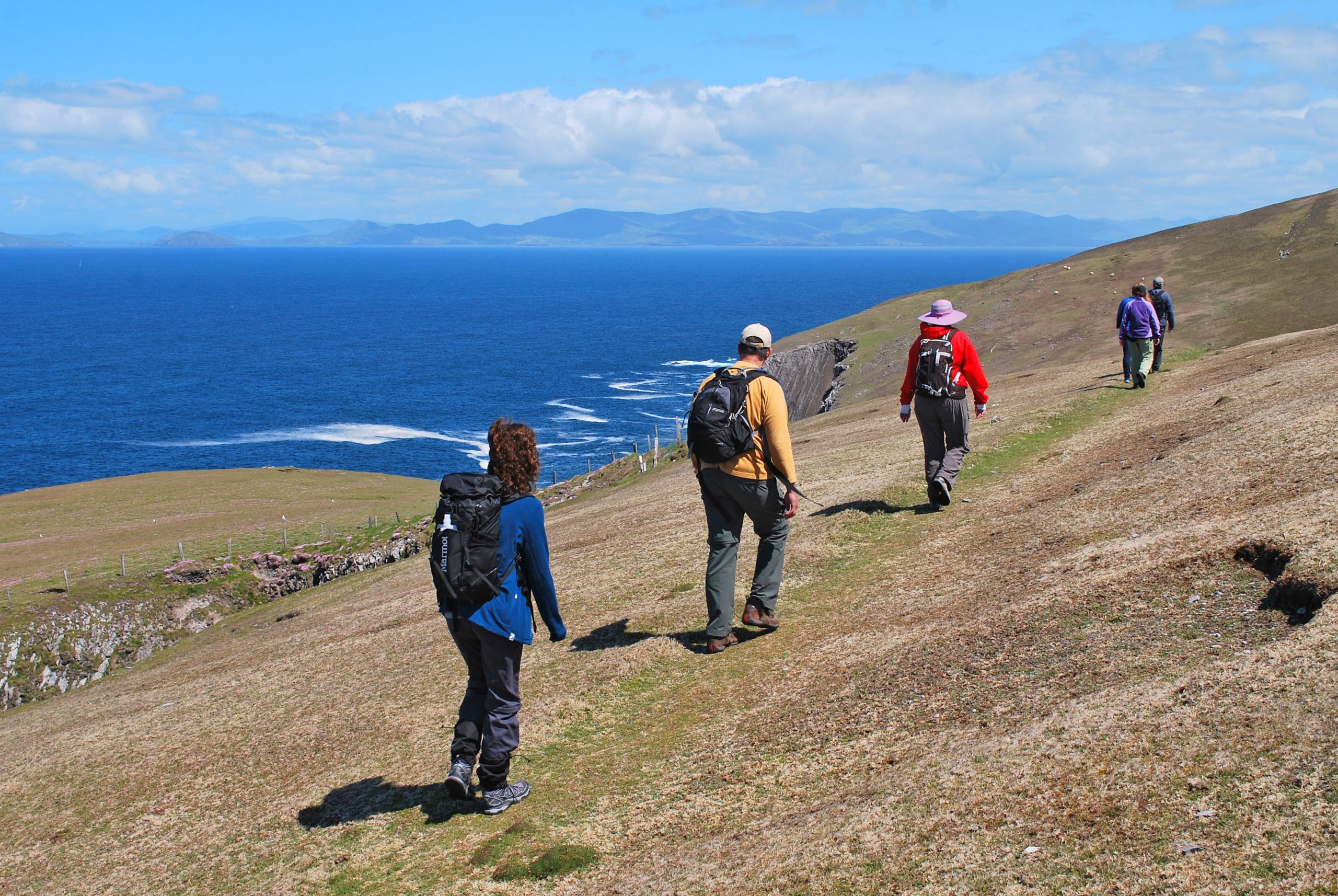 Persone che camminano in fila su un sentiero collinare con l’oceano sullo sfondo, trekking in Irlanda