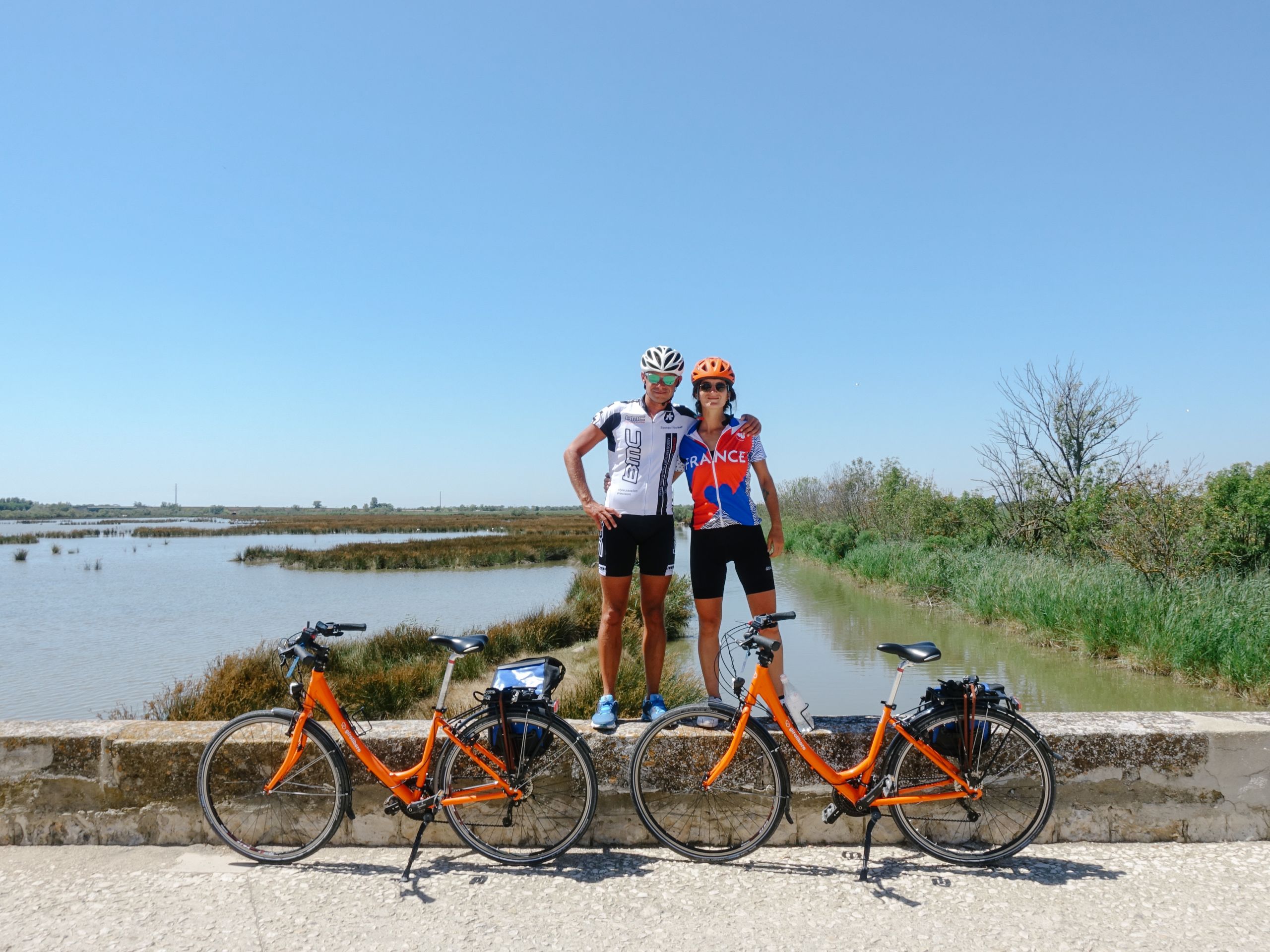 Couple of cyclists with Girolibero bikes celebrating on a bike path, Mediterranean landscape, France.