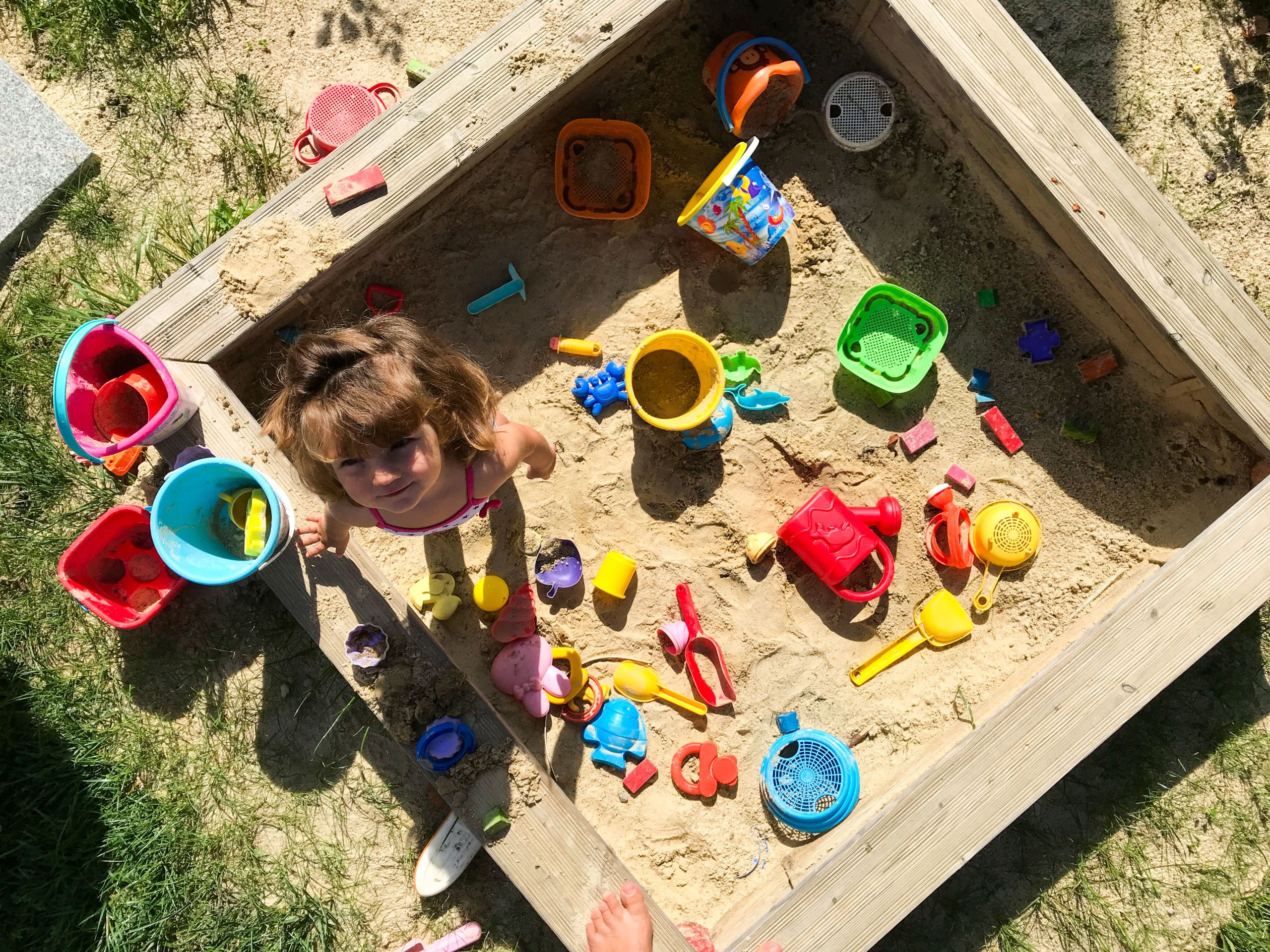 Bambina sorridente intenta a giocare con la sabbia, cestelli e palette colorate, vacanza per famiglie, Austria