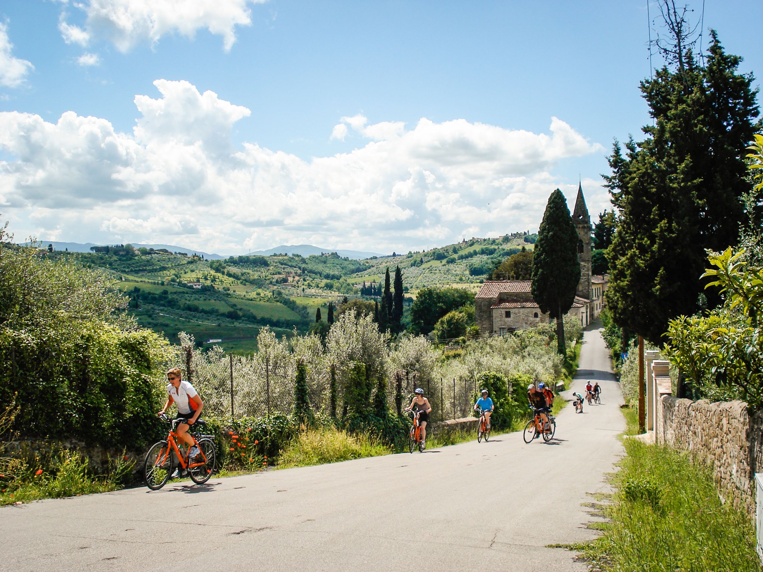 Gruppo di ciclisti con caschetto, bici Girolibero, paesaggio collinare verde in Toscana, Italia