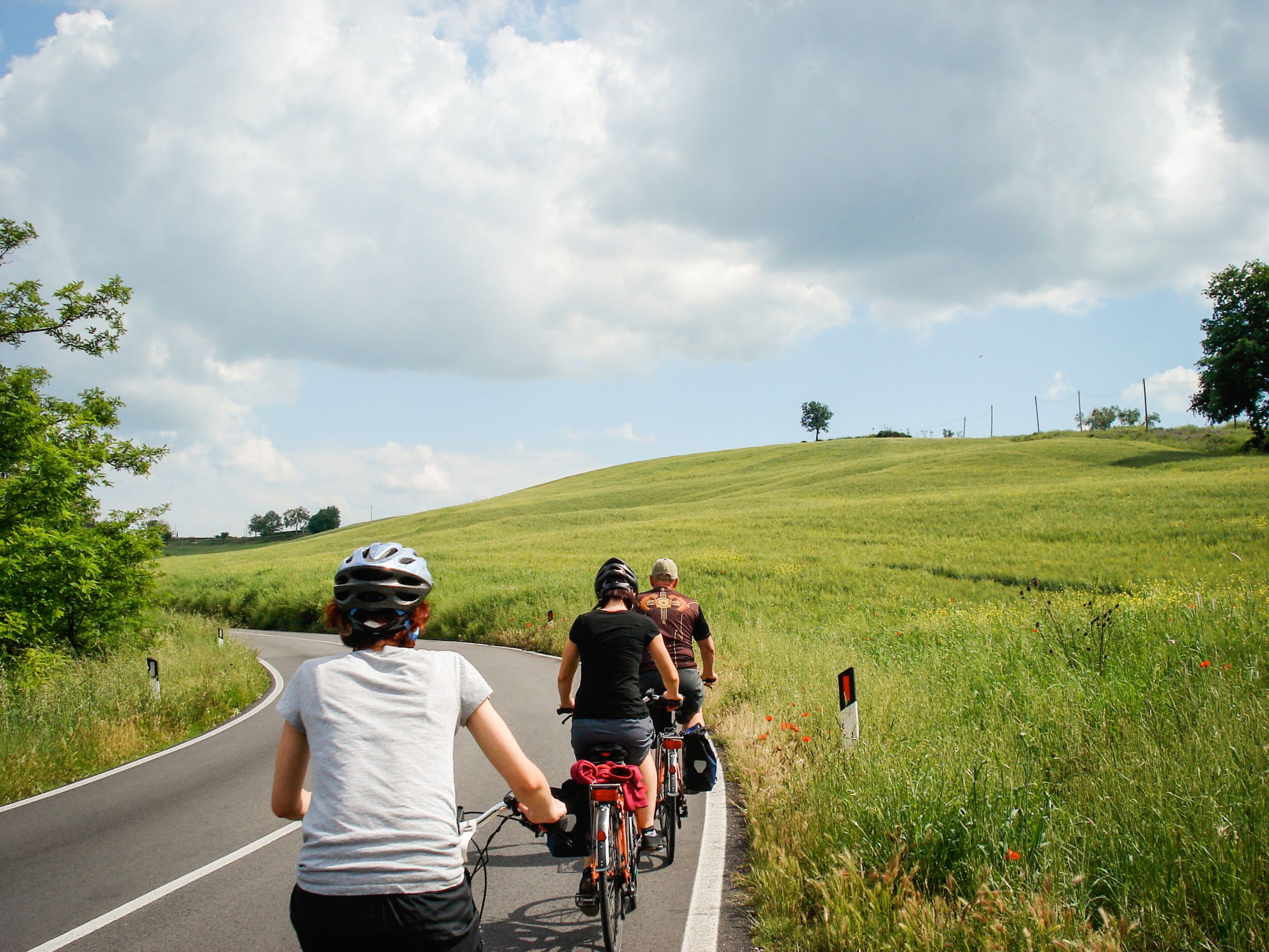 Gruppo di ciclisti con caschetto, bici Girolibero, paesaggio collinare verde in Toscana, Italia