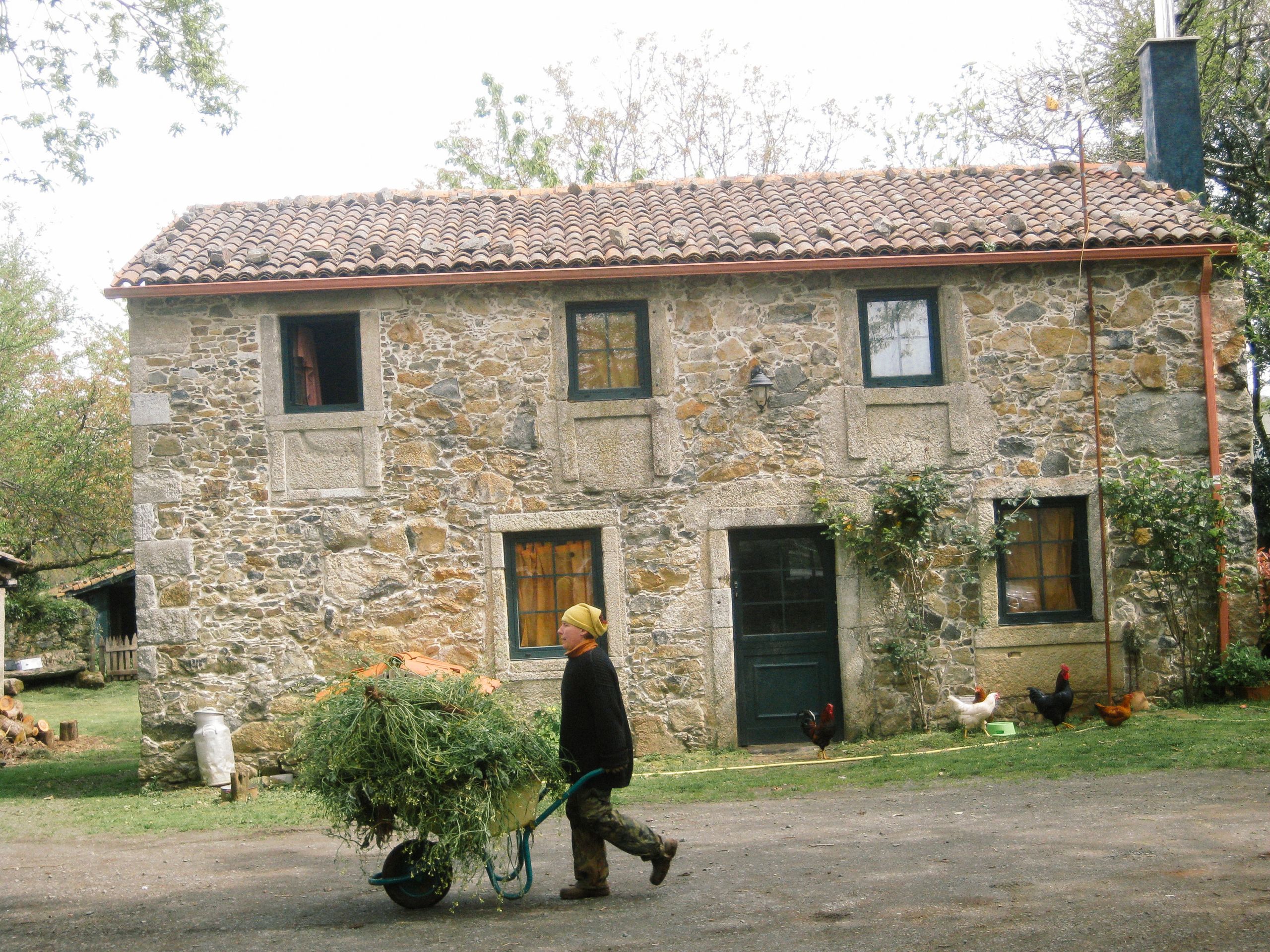 Contadino al lavoro davanti a una vecchia casa rurale in pietra