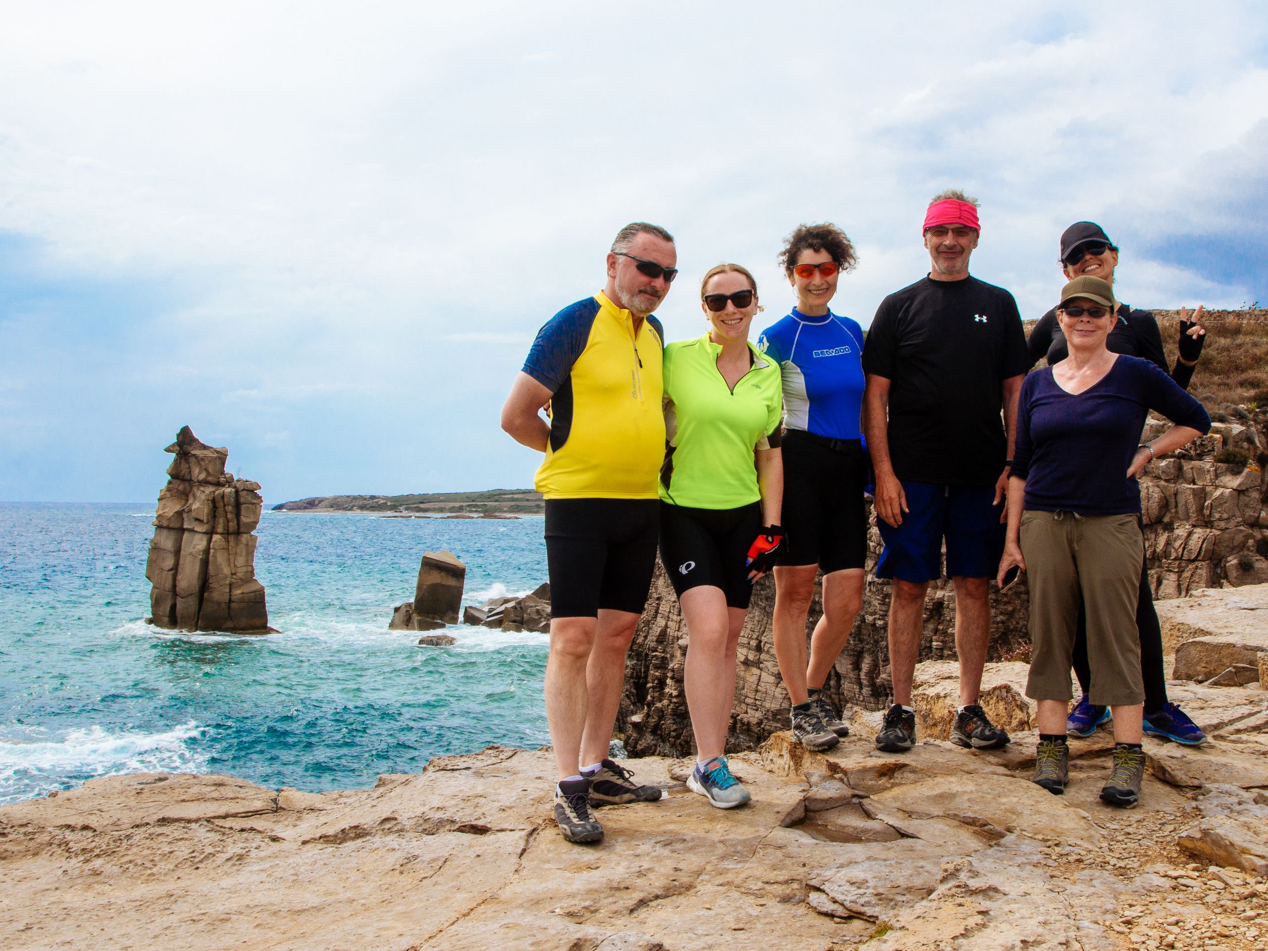 Gruppo di cicloturisti in posa davanti al mare con scogliere, Sardegna