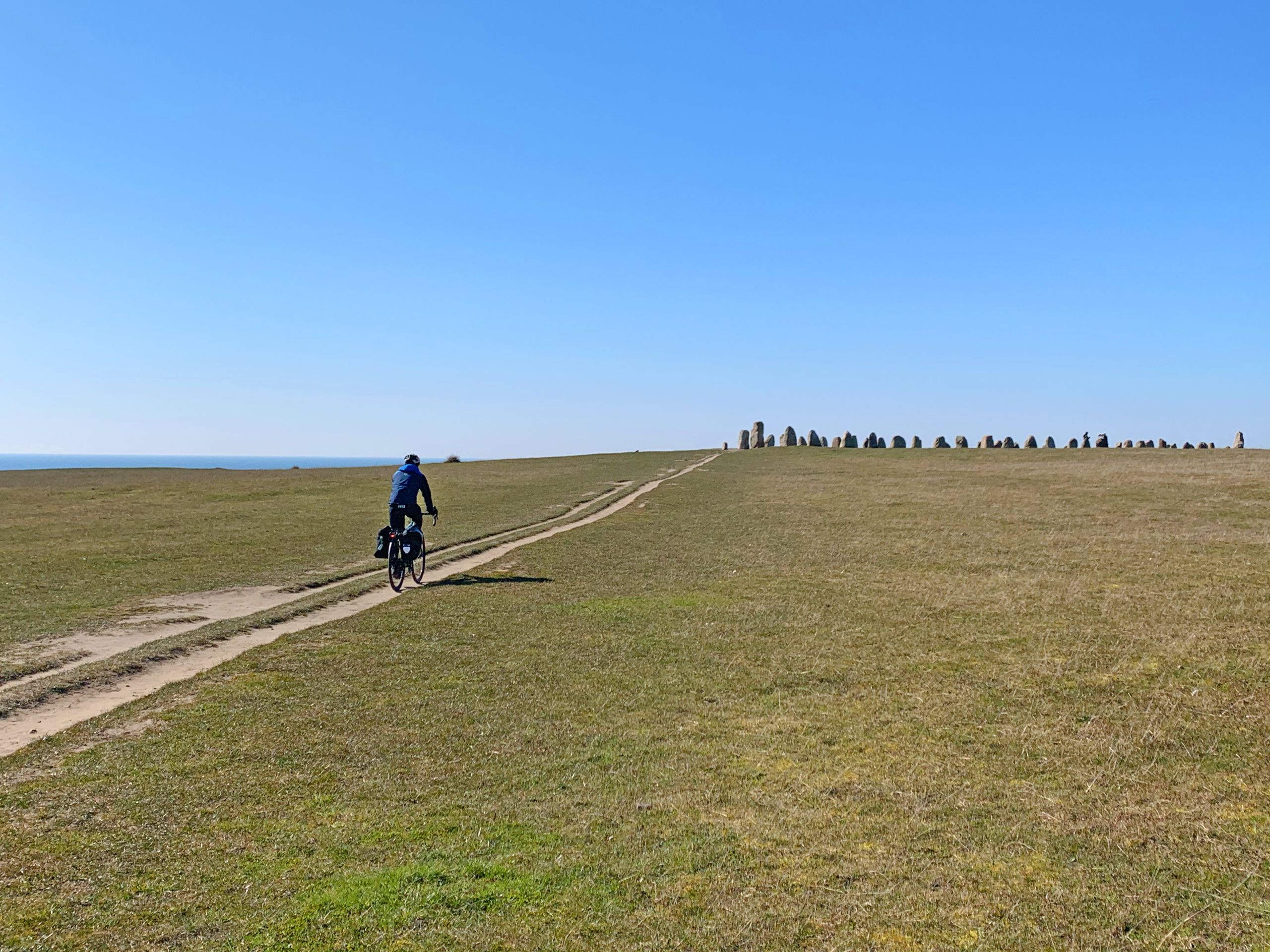 Pianura erbosa nella riserva naturale di Ales Stenar, Svezia, con ciclista che pedala su un sentiero