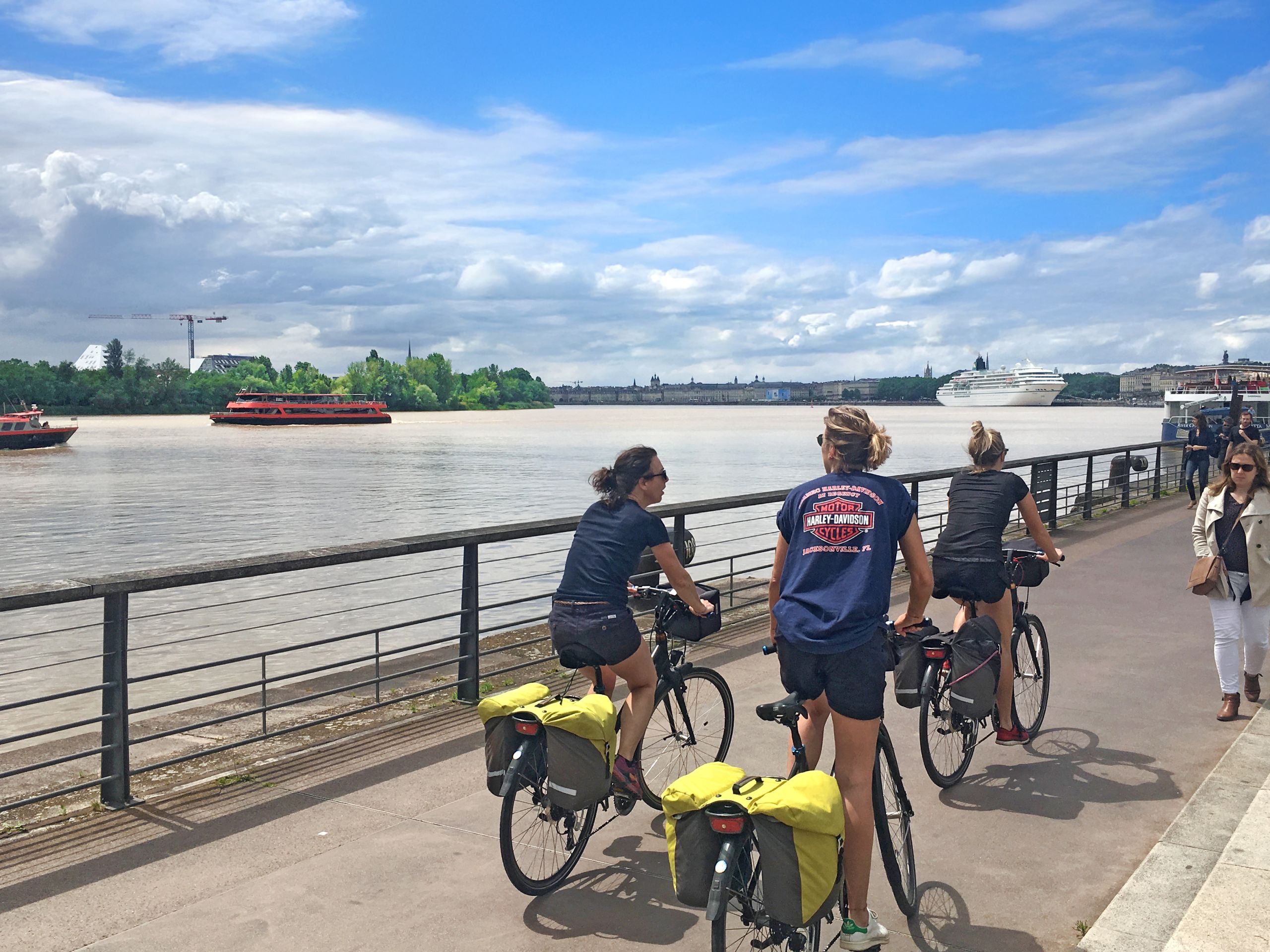 Ciclisti lungo la Garonna a Bordeaux, Francia, con vista sui palazzi storici del lungofiume.