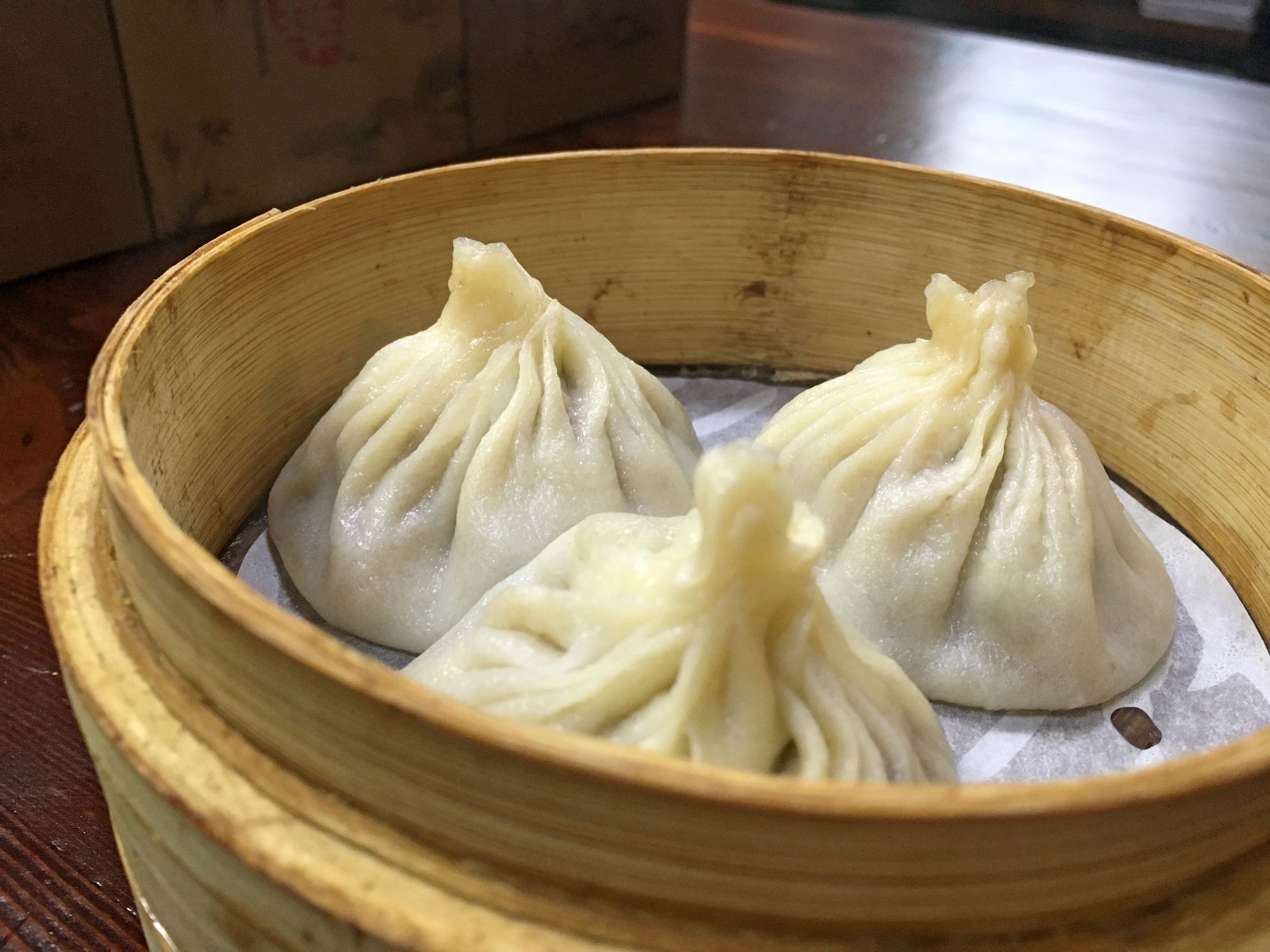 Cestino in bambù con ravioli al vapore cinesi xiaolongbao su tavolo da ristorante.