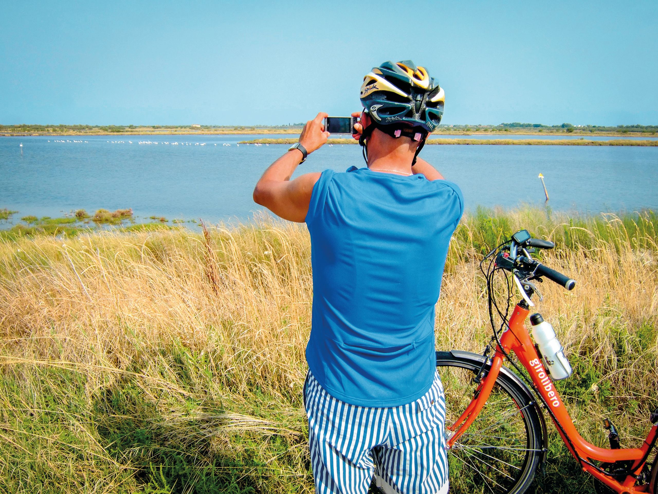 Cyclist travelling with Girolibero bike takes a photo by the sea, Venetian lagoon