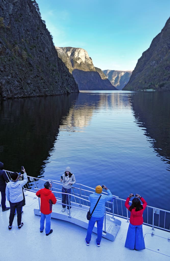 Turisti su una nave da crociera mentre ammirano il paesaggio montuoso del Nærøyfjord, sito patrimonio UNESCO.