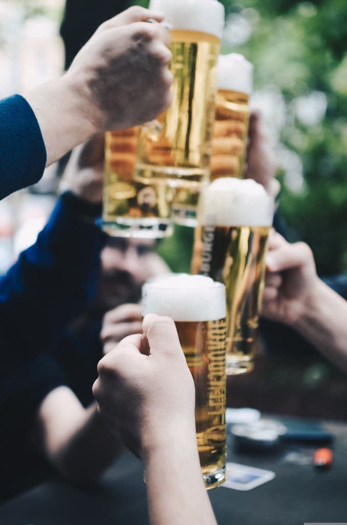 Brindisi in biergarten tedesco: mani che sollevano boccali di birra chiara spumeggiante all’aria aperta.