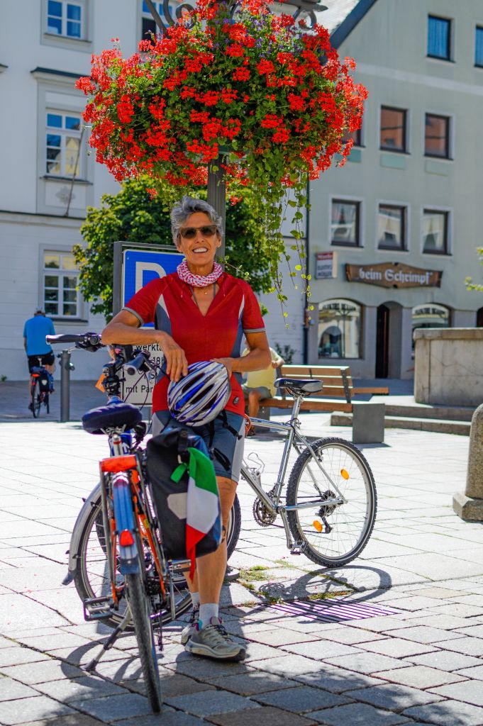 Ciclista in una piazza fiorita di una città lungo la Romantische Strasse, Germania, con decorazioni floreali.