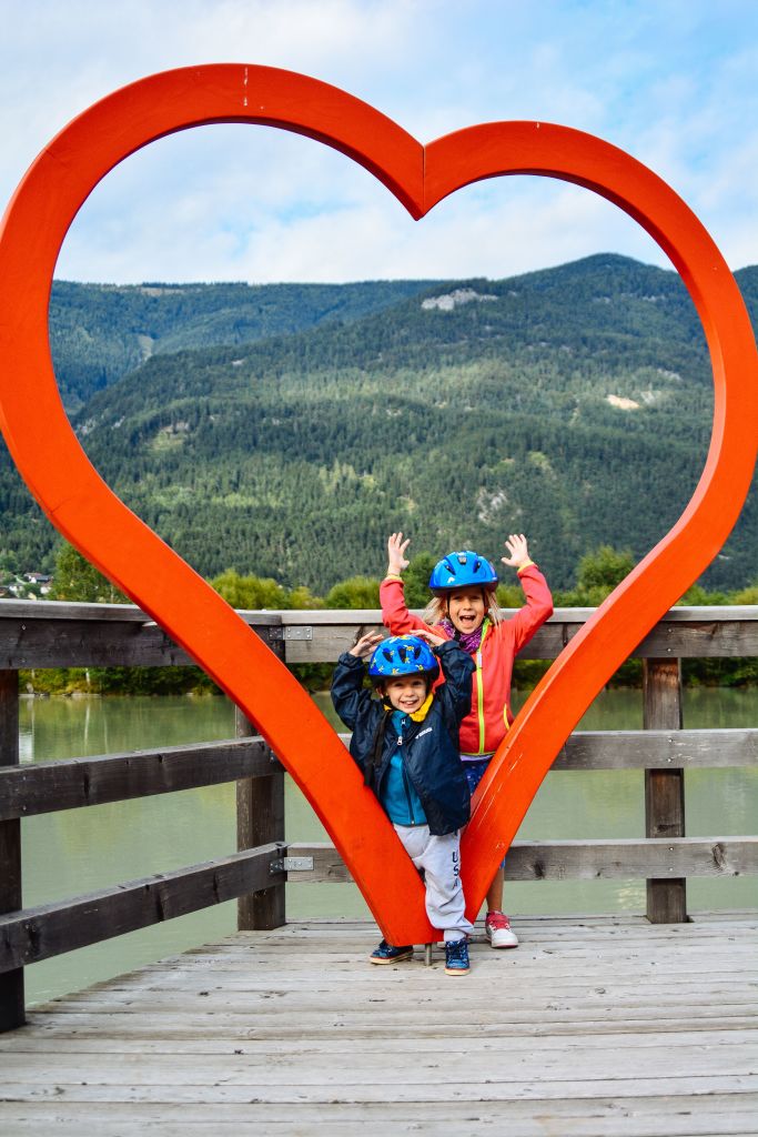 Bambini dentro un installazione a forma di cuore, angolo, paesaggio di montagna, ciclabile Drava