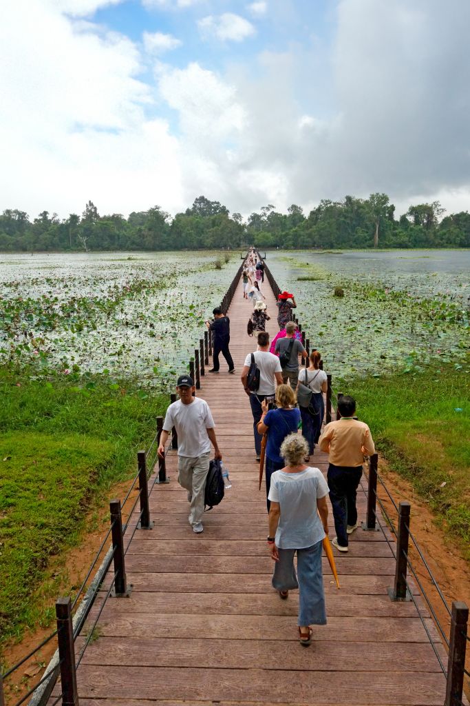 Turisti che percorrono la passerella galleggiante sul fossato e lago di ninfee di Angkor Wat