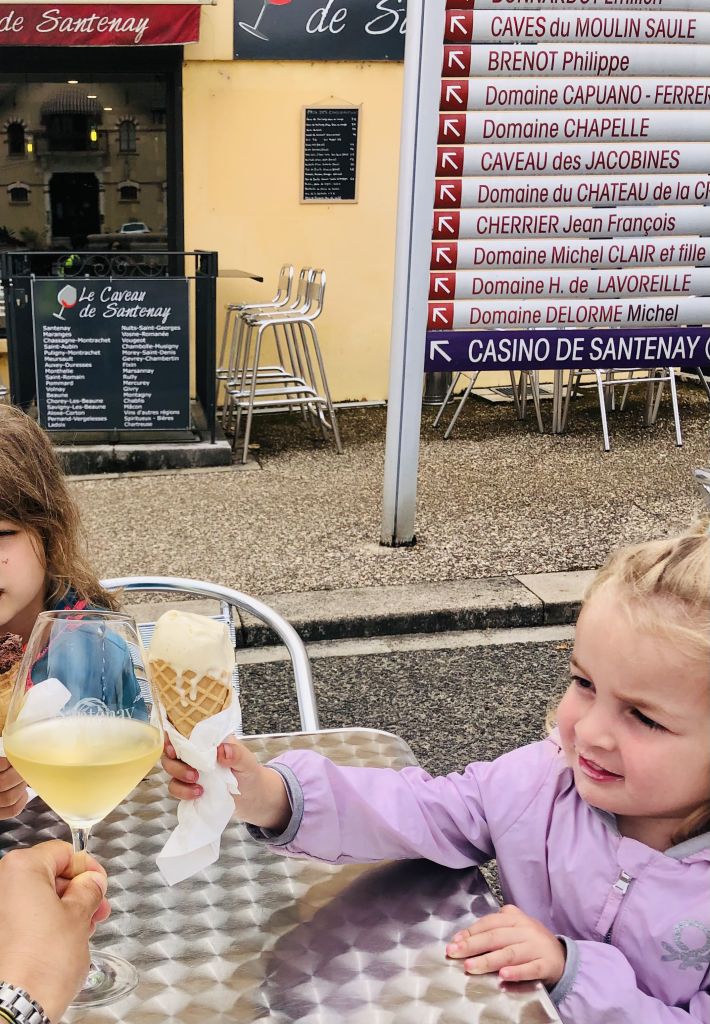 Bambina che mangia un gelato seduta a un tavolino in una piazza francese e donna che beve un calice di vino.