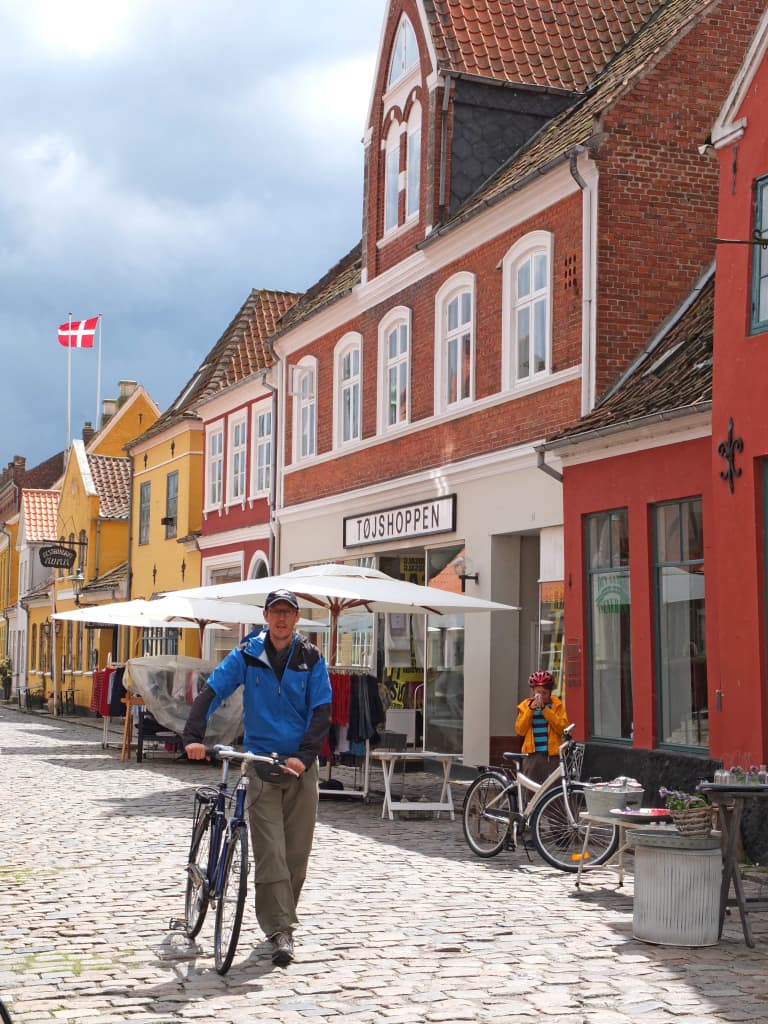 Cicloturista nel centro storico di Ærøskøbing, case pastel‑color e bandiera danese sull’isola di Ærø.