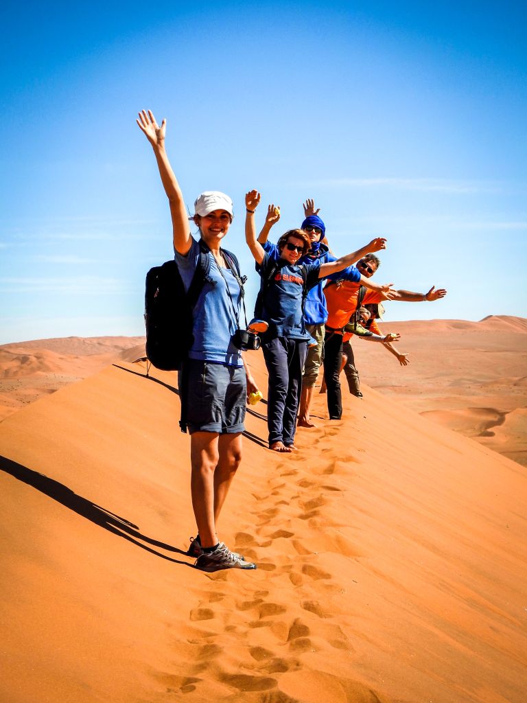 Namibia, viaggi di gruppo organizzati da "Girolibero", gruppo di persone che camminano su dune di sabbia rossa nel deserto del Namib