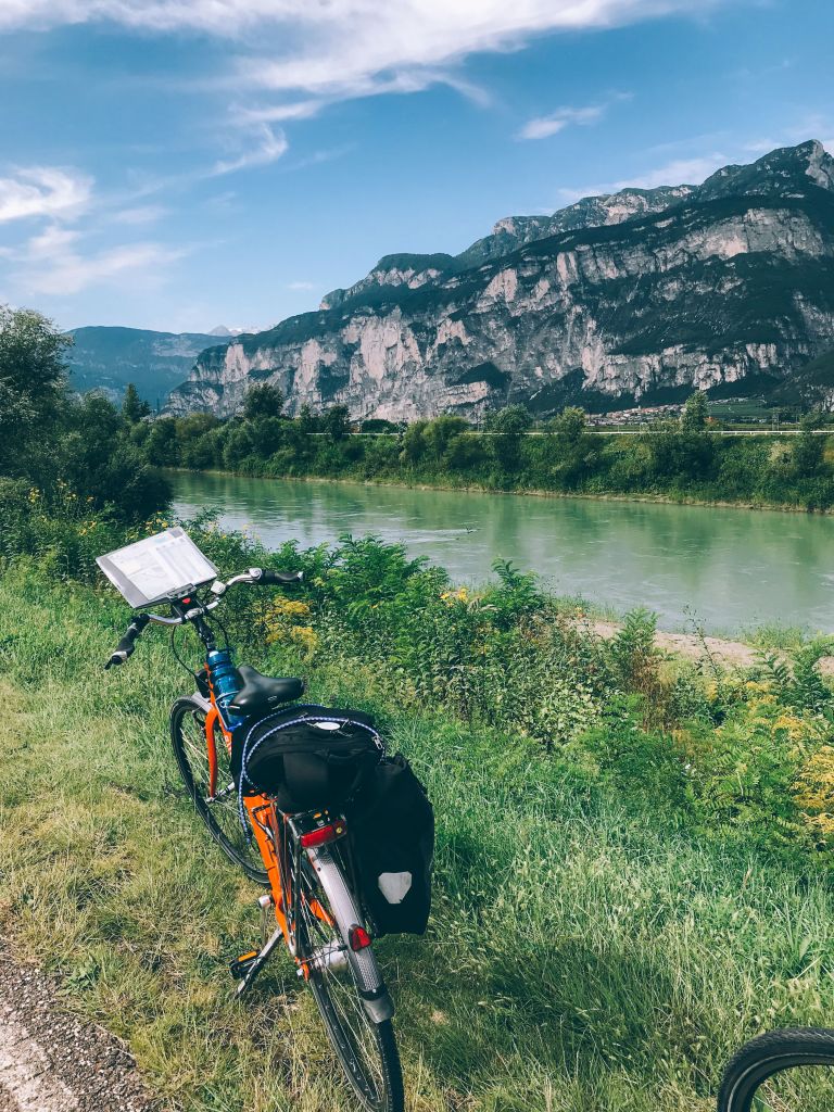 Bici "Girolibero" parcheggiata con fiume Adige e montagne sullo sfondo
