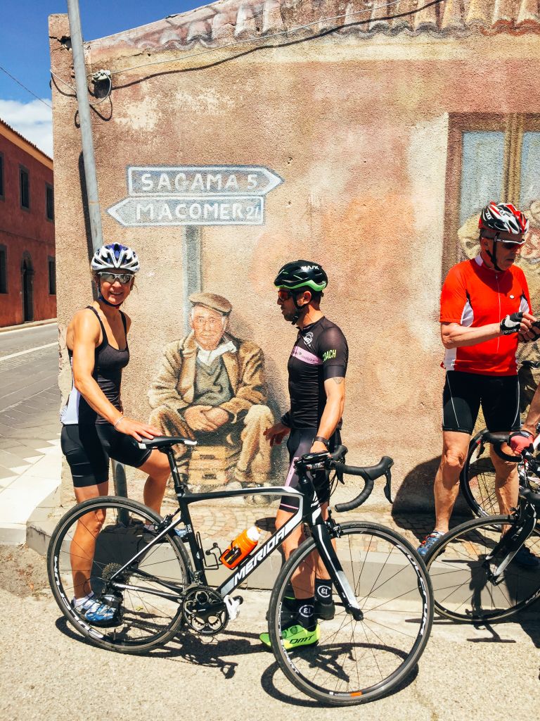 Gruppo di ciclisti in sosta davanti a un edificio storico, borgo italiano in Sardegna