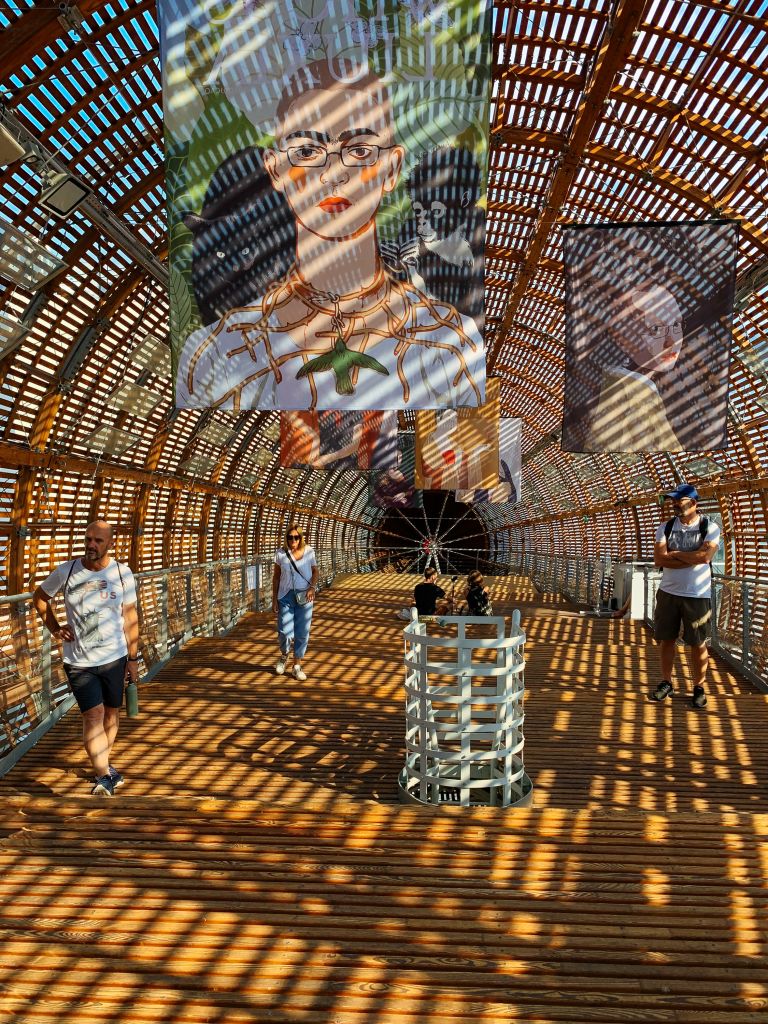 Interno di una sala di un museo, installazione artistica in primo piano, volto di donna con giochi di luce e ombre